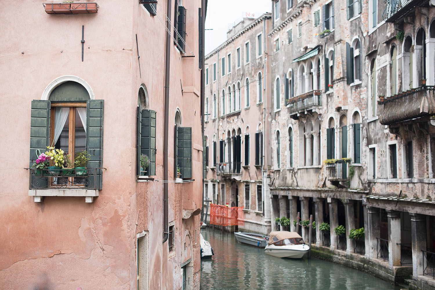 Photo of pink buildings with green and white shutters facing onto canal in Venice
