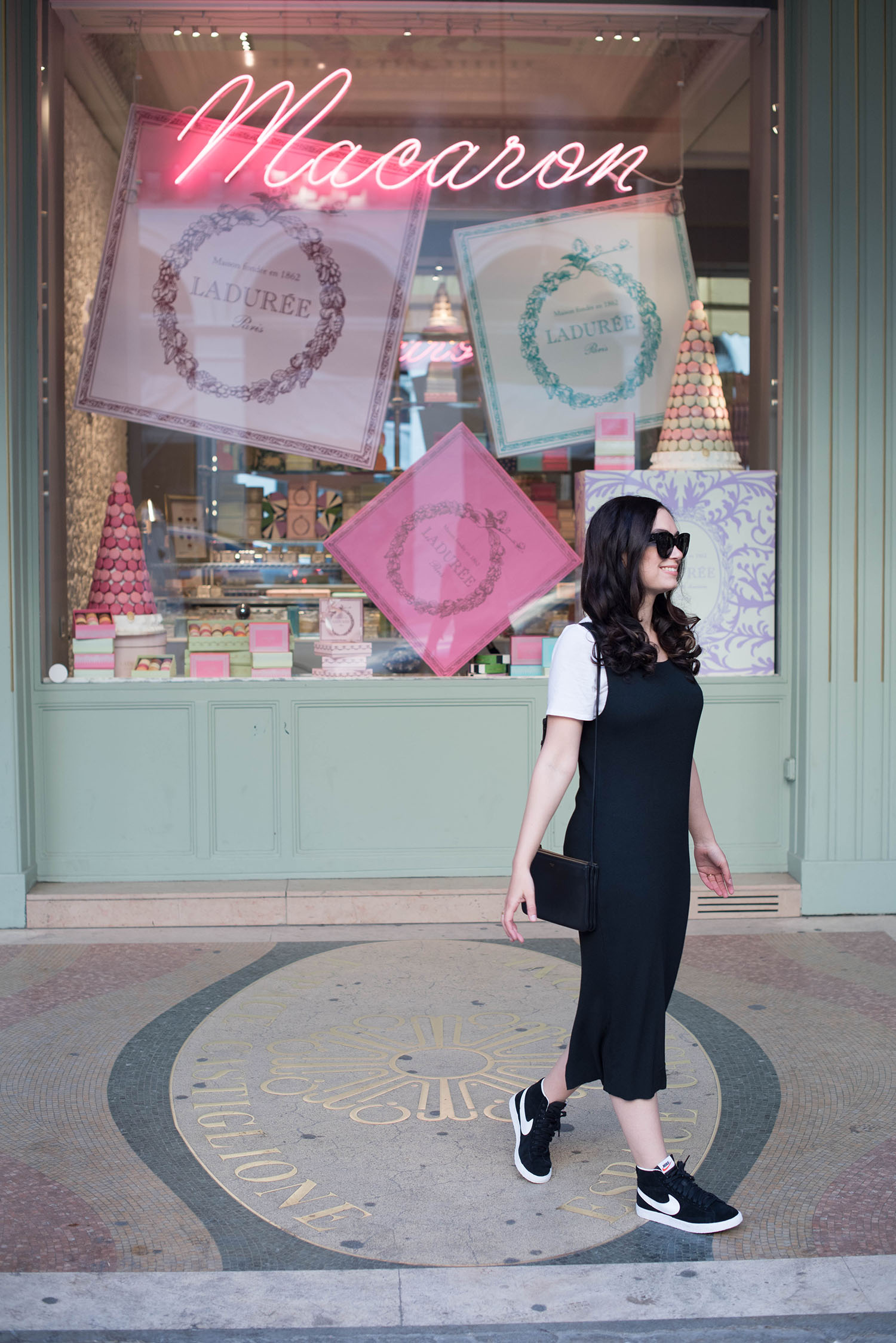 Photo of lifestyle blogger Cee Fardoe at Laduree in Paris, wearing a black pinafore dress and Nike sneakers