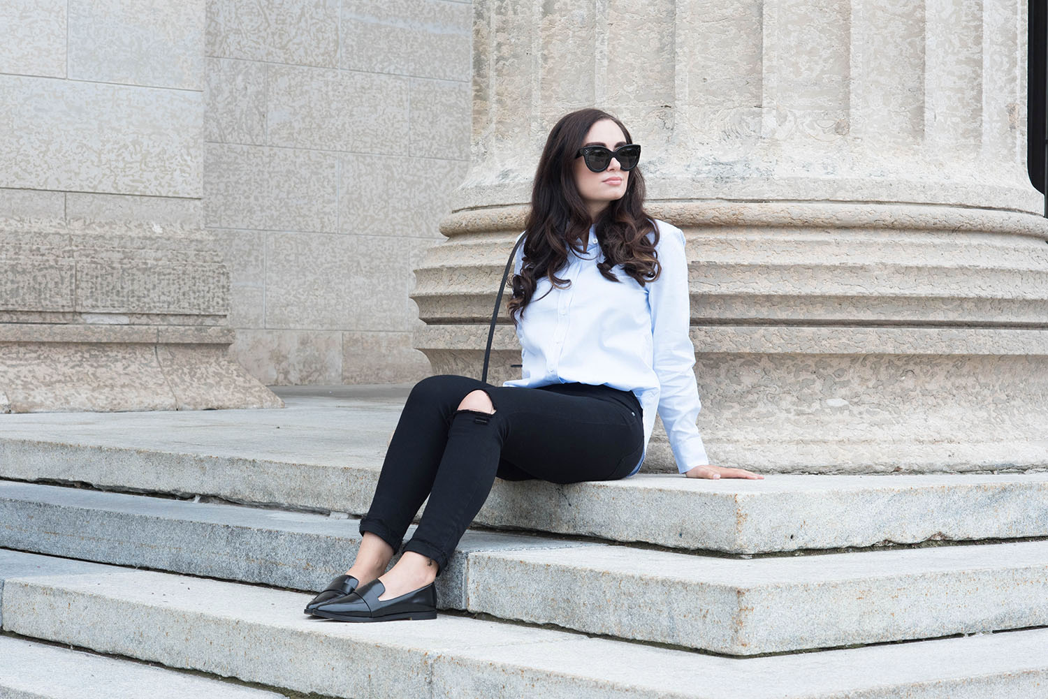 Canadian fashion blogger Cee Fardoe of Coco & Vera sits on the steps of the Manitoba legislature wearing Celine Audrey sunglasses and Paige jeans