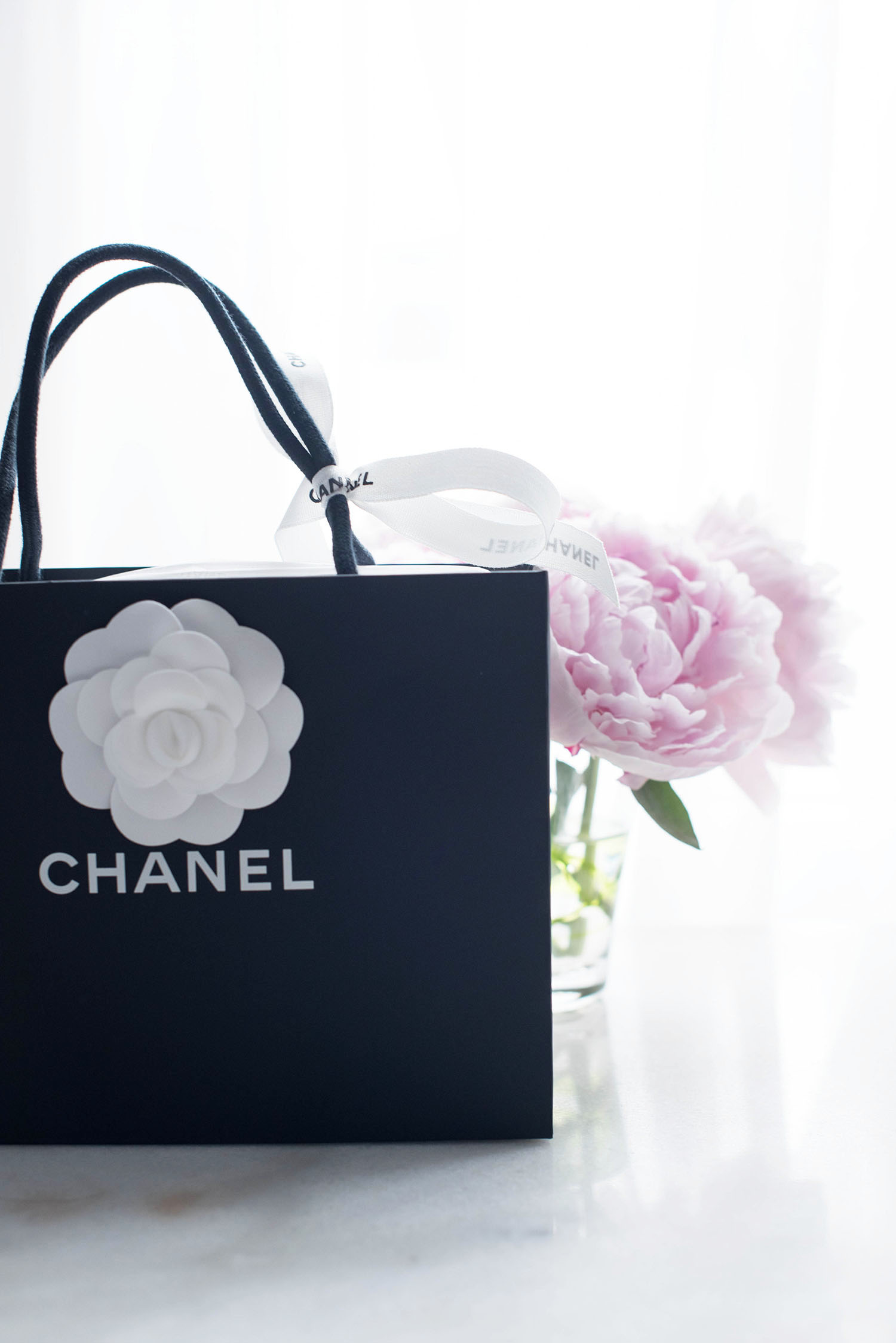 A Chanel shopping bag displayed with pink peonies on a marble table by fashion blogger Cee Fardoe of Coco & Vera