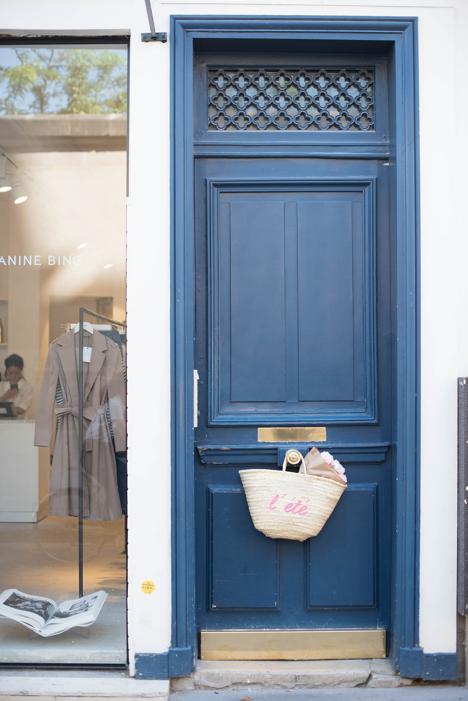 A Sezane straw tote full of pink peonies hangs on a blue door in le Marais, captured by travel blogger Cee Fardoe of Coco & Vera