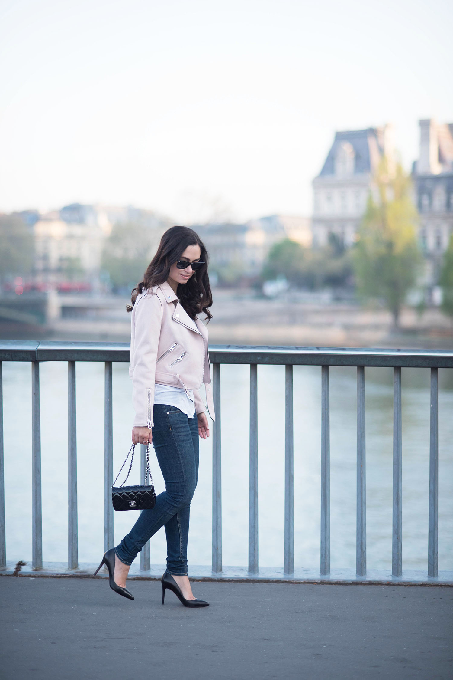 Fashion blogger Cee Fardoe of Coco & Vera walks in front of Hotel de Ville in Paris wearing a Zara pink moto jacket