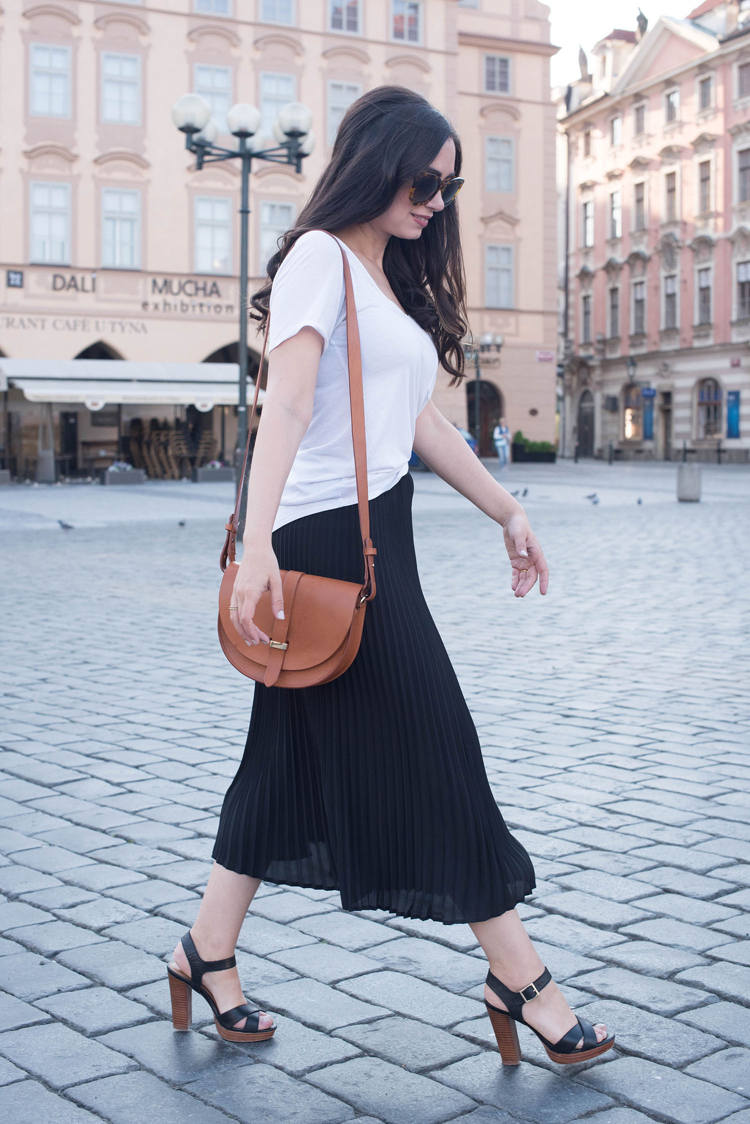 Canadian fashion blogger Cee Fardoe of Coco & Vera walks through Old Town Square in Prague carrying a Sezane Claude bag and wearing a black Aritzia skirt