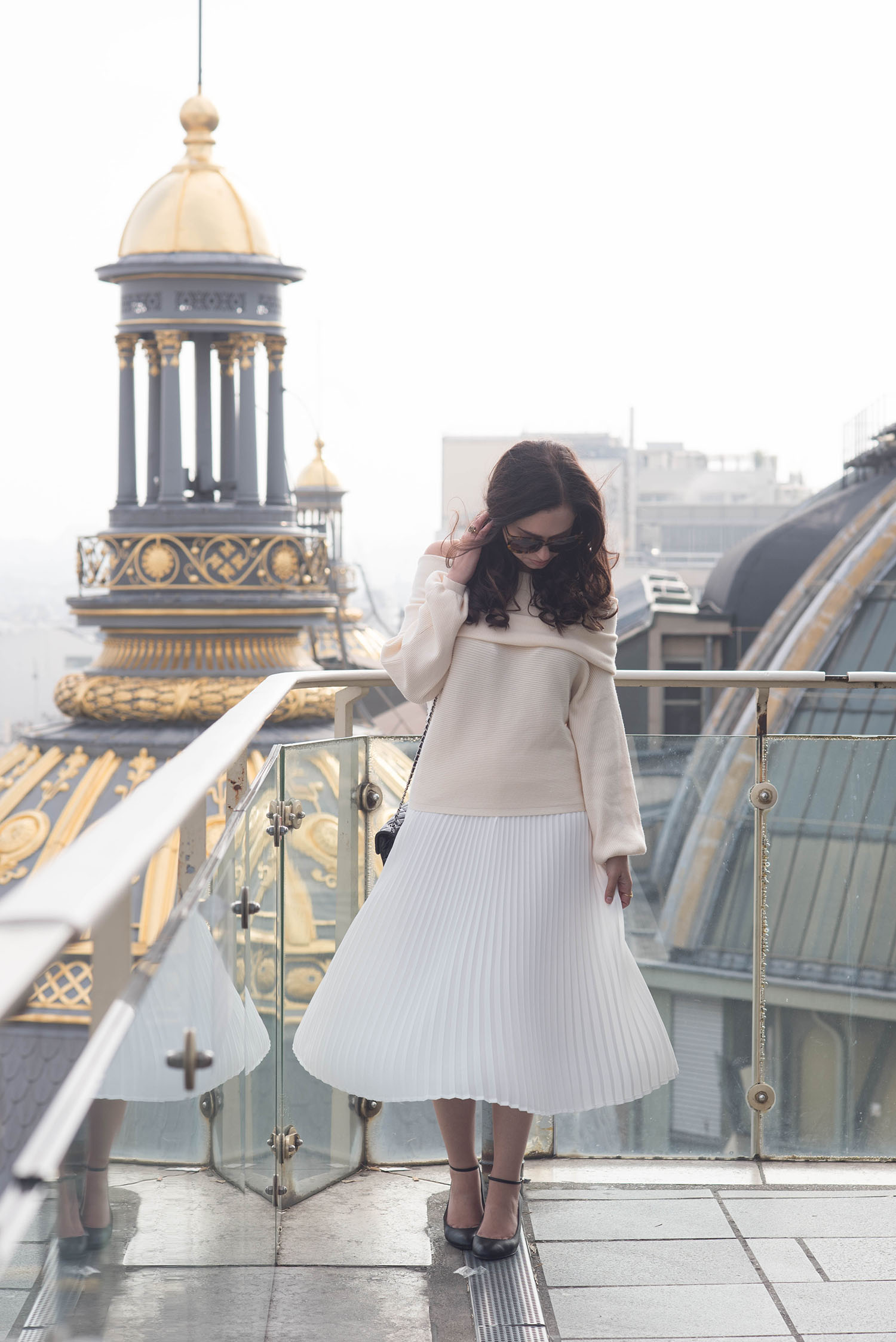 Fashion blogger Cee Fardoe of Coco & Vera stands on the rooftop of Paris department store Printemps wearing a Zara blush sweater and Aritzia pleated skirt