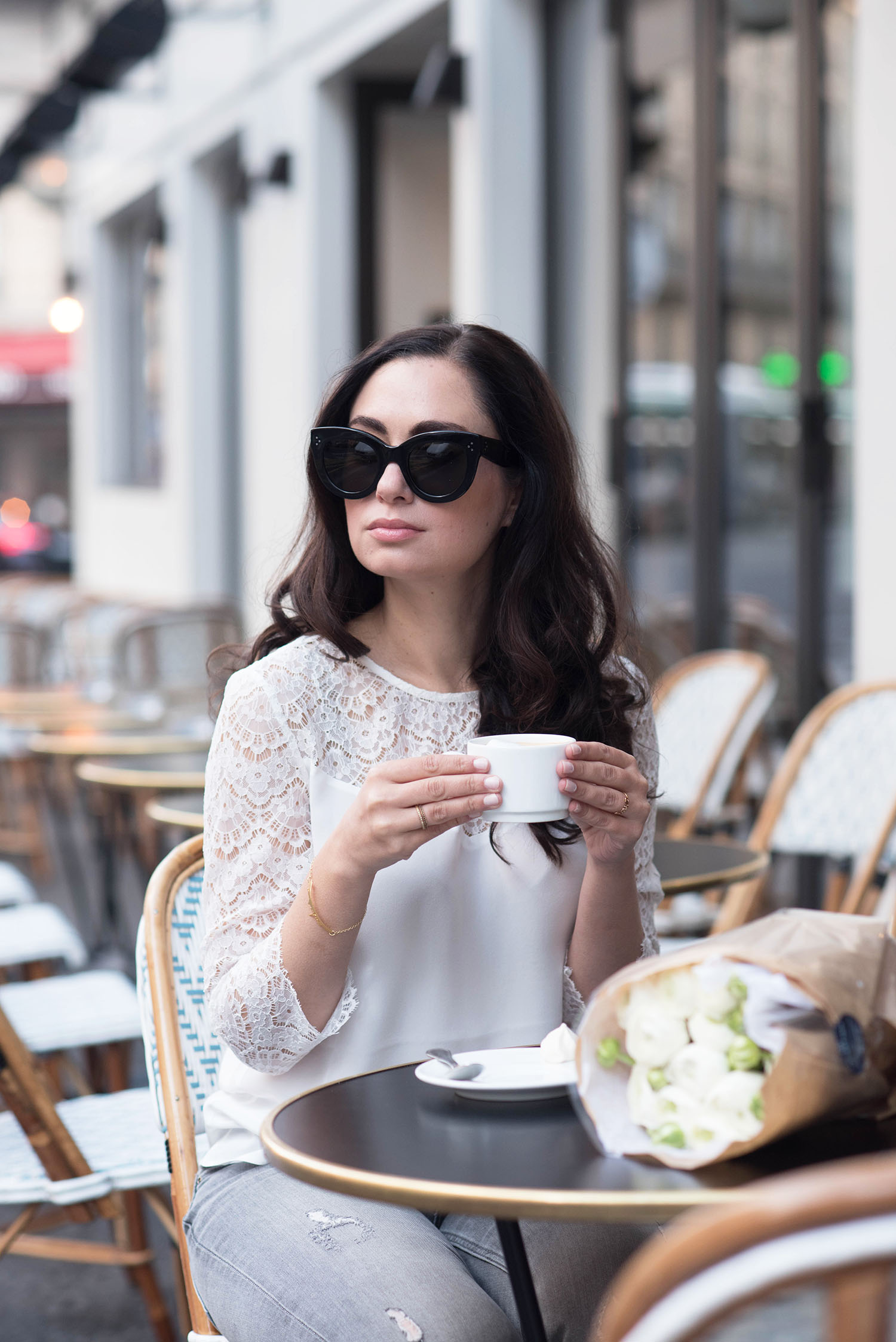 Winnipeg fashion blogger Cee Fardoe of Coco & Vera sits outside at Maison Marie in Paris, holding her coffee cup and wearing a Sezane blouse