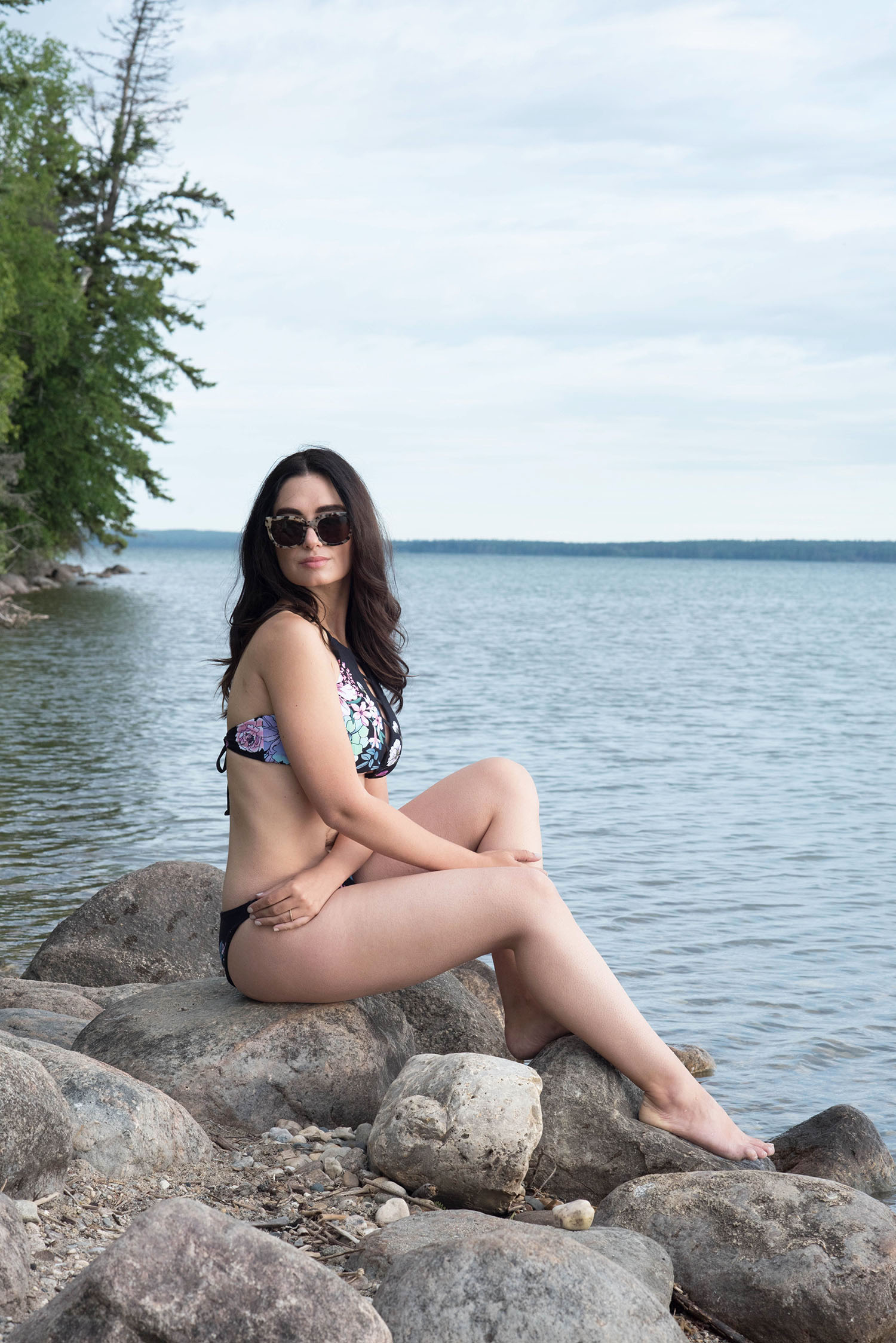 Canadian fashion blogger Cee Fardoe of Coco & Vera sits on a rocky beach wearing a floral O'Neill bikini