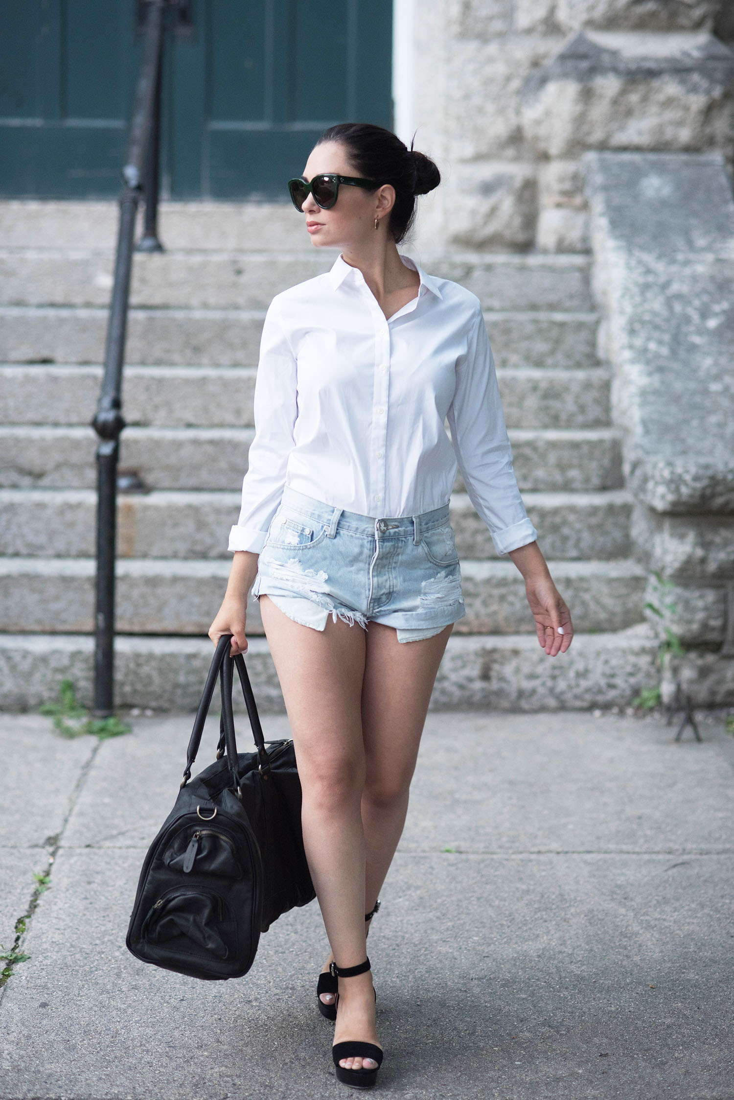 Canadian fashion blogger Cee Fardoe of Coco & Vera walks down the street wearing One Teaspoon denim shorts and carrying a Mahi Leather duffle bag