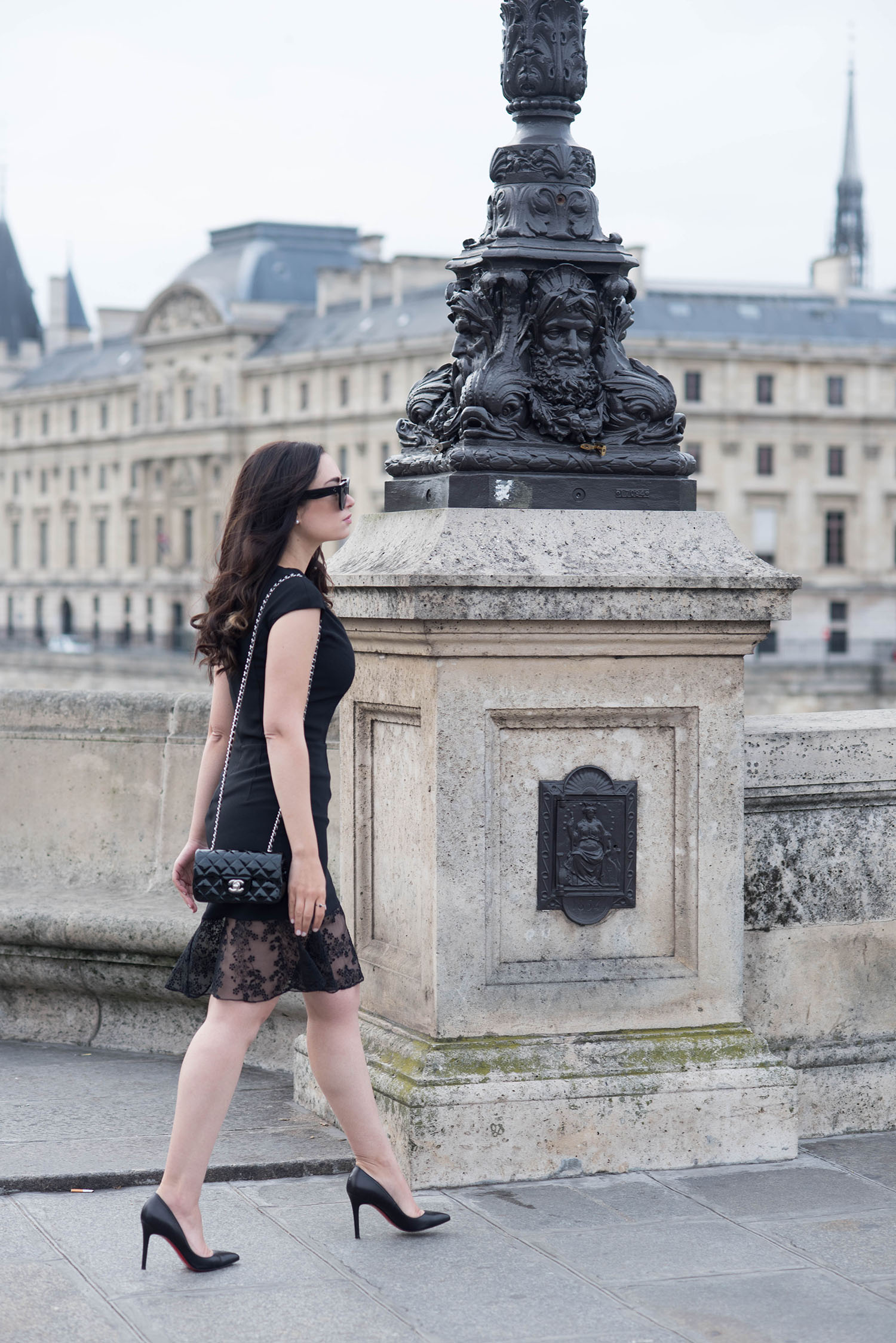 Fashion blogger Cee Fardoe of Coco & Vera walks on Pont-Neuf in Paris wearing a Carven LBD and Christian Louboutin Pigalle pumps