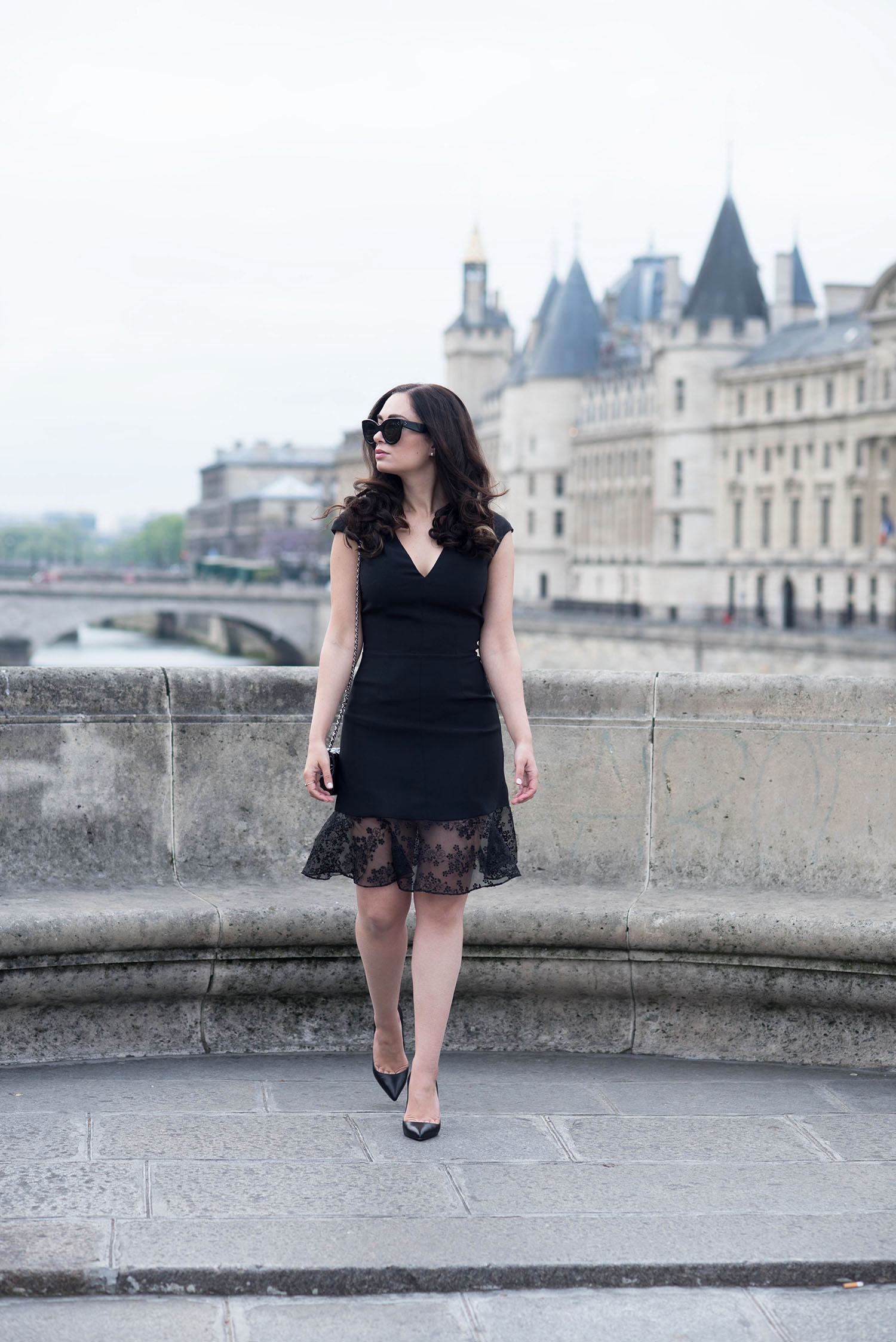 Fashion blogger Cee Fardoe of Coco & Vera walks on Pont Neuf in Paris wearing a black Carven dress and Celine Audrey sunglasses