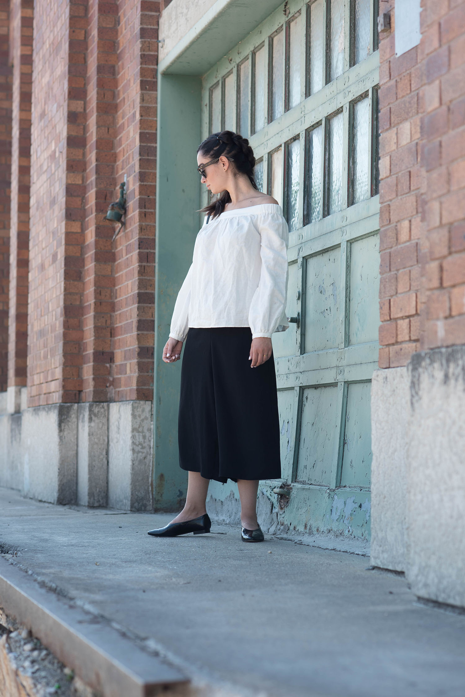 Top fashion blogger Cee Fardoe of Coco & Vera walks in the Winnipeg Exchange District wearing Zara patent flats, Aritzia black culottes and Rayban sunglasses