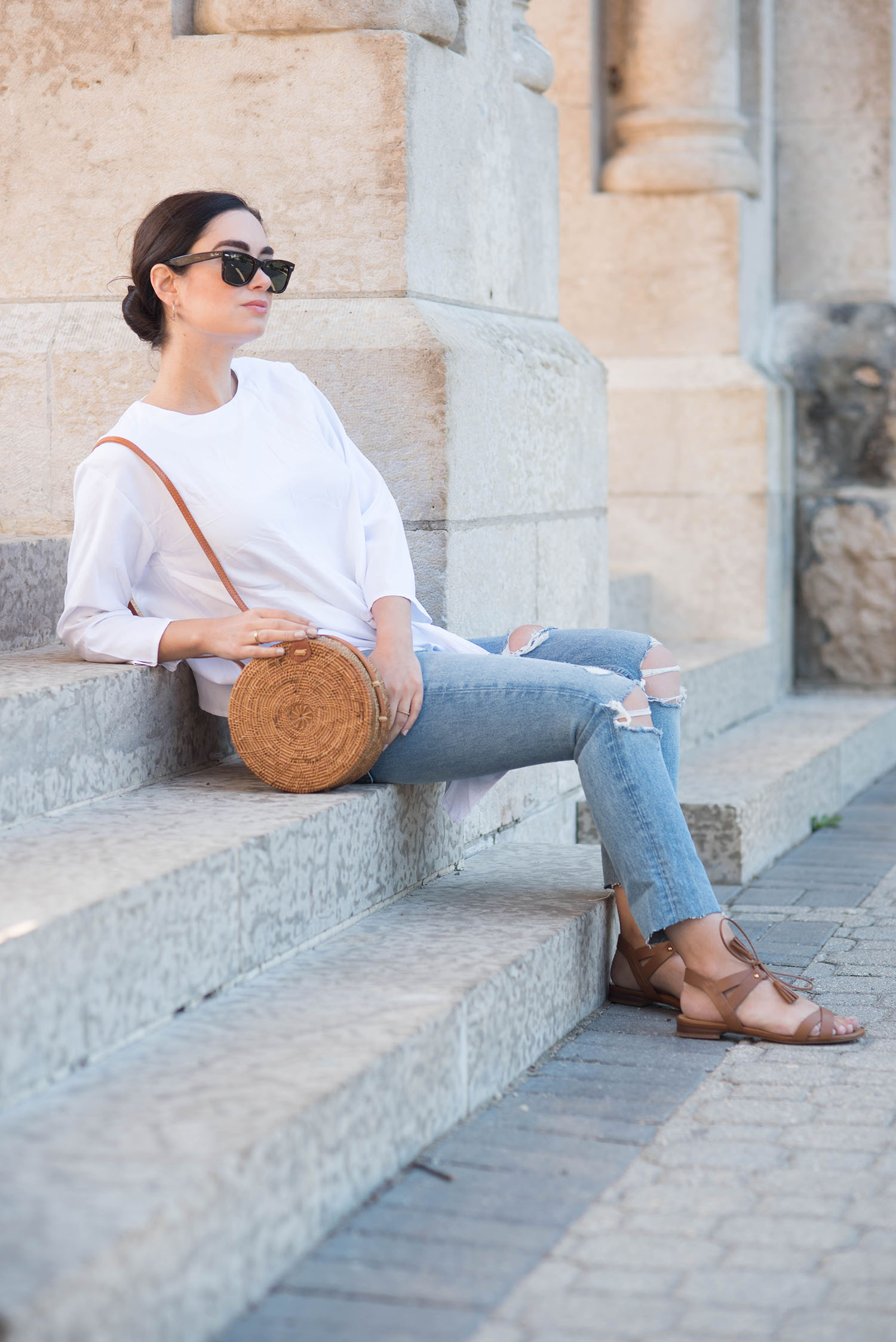 Fashion blogger Cee Fardoe of Coco & Vera sits at St. Boniface cathedral wearing a Missy Empire Aracely blouse, Grlfrnd Karolina blue jeans and holding an Ellen James rattan bag