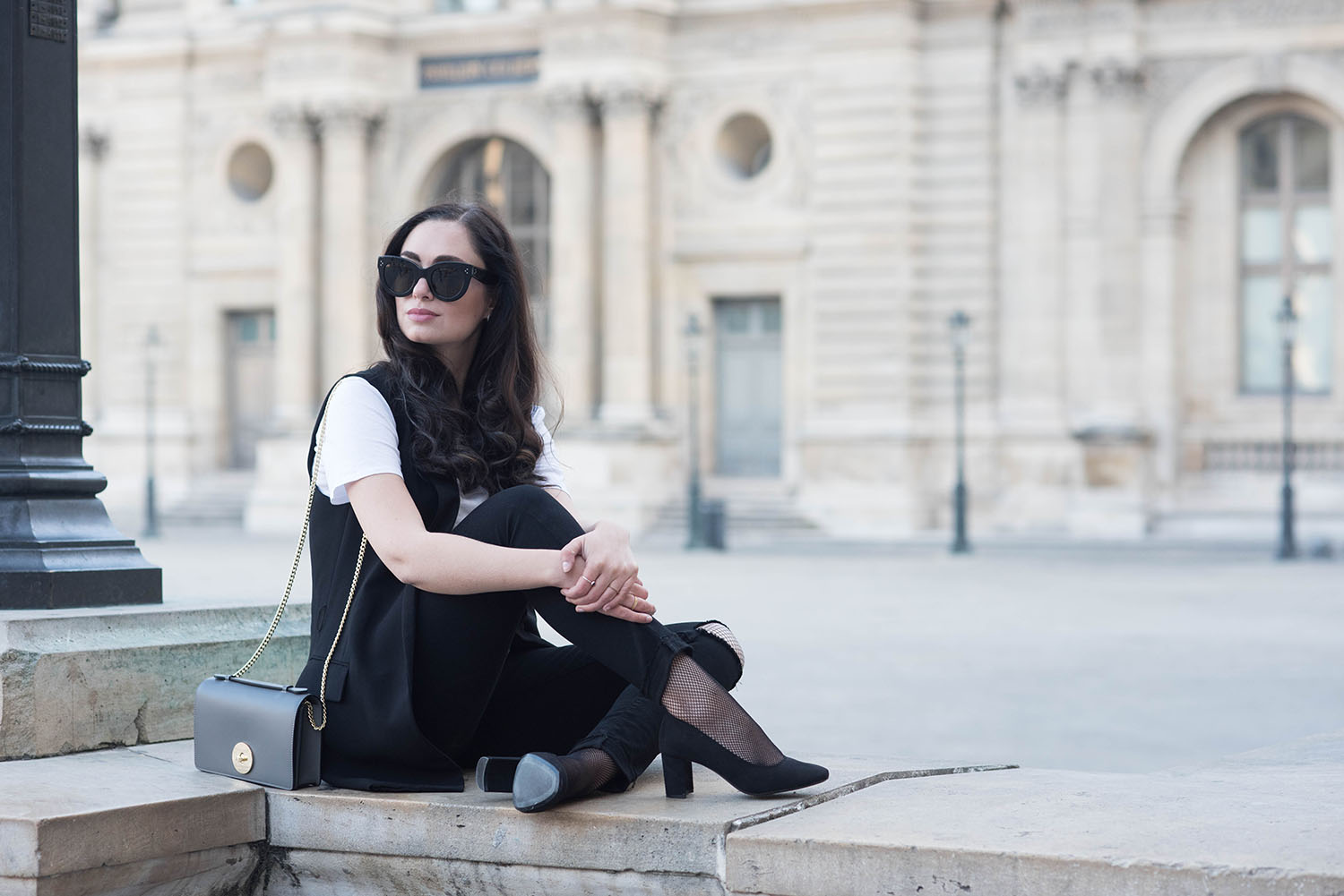 Winnipeg fashion blogger Cee Fardoe of Coco & Vera sits on the grounds of the Louvre wearing black Paige jeans and H&M block heels