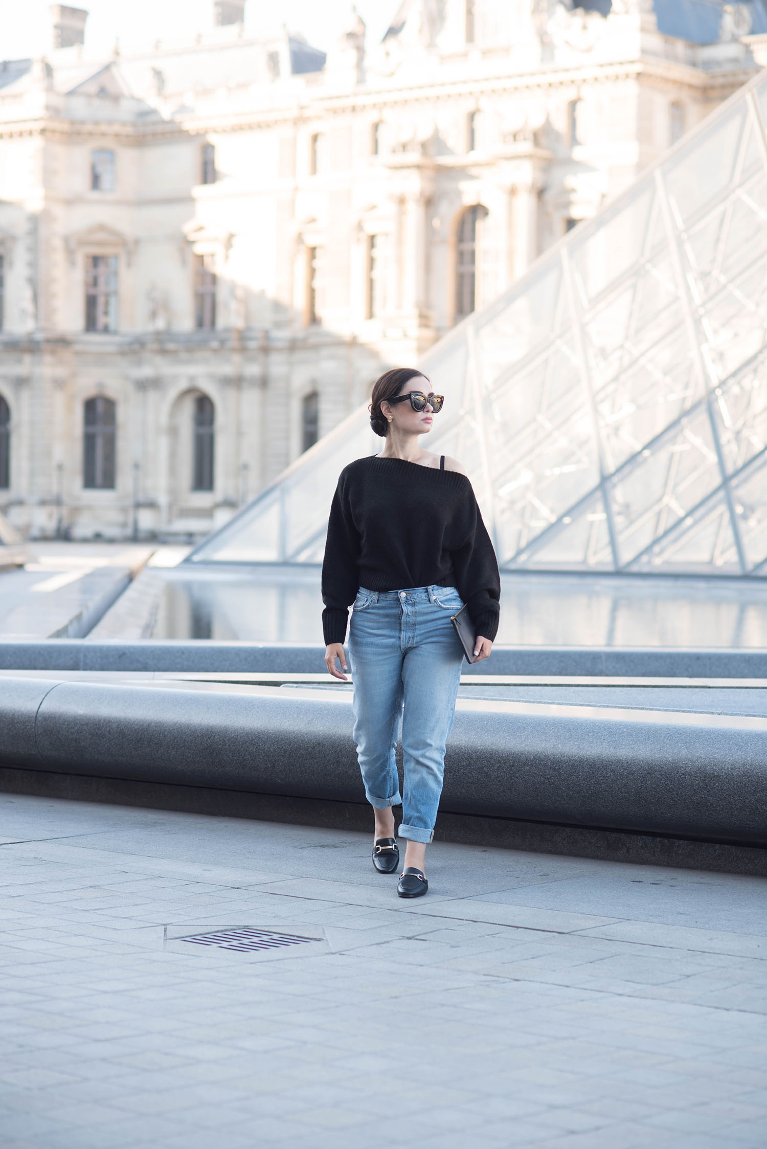 Fashion blogger Cee Fardoe of Coco & Vera walks in front of the Louvre pyramid wearing Zara boyfriend jeans and carrying a Celine clutch
