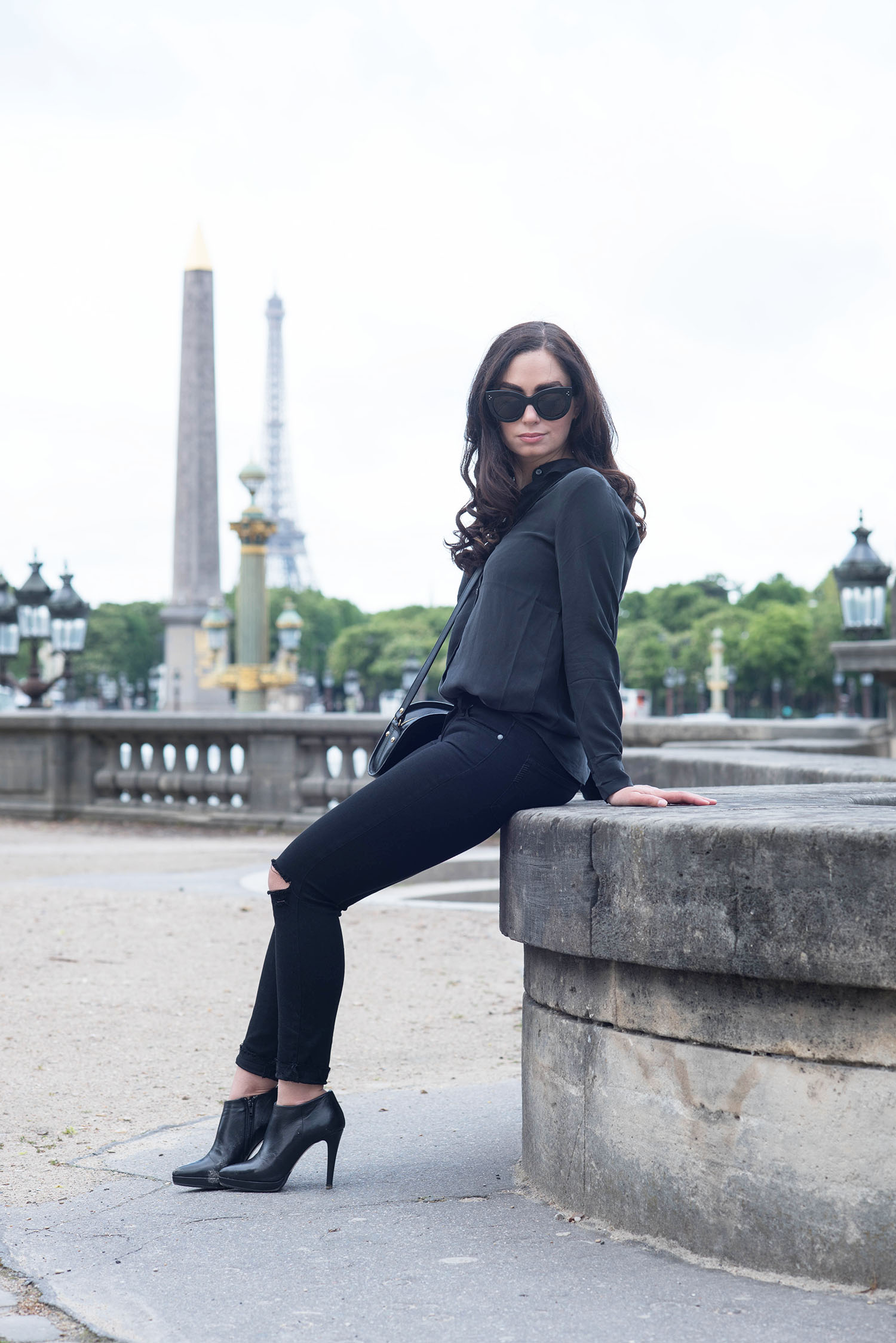 Fashion blogger Cee Fardoe of Coco & Vera sits at Place de la Concorde in Paris, wearing an Everlane silk blouse and Paige jeans