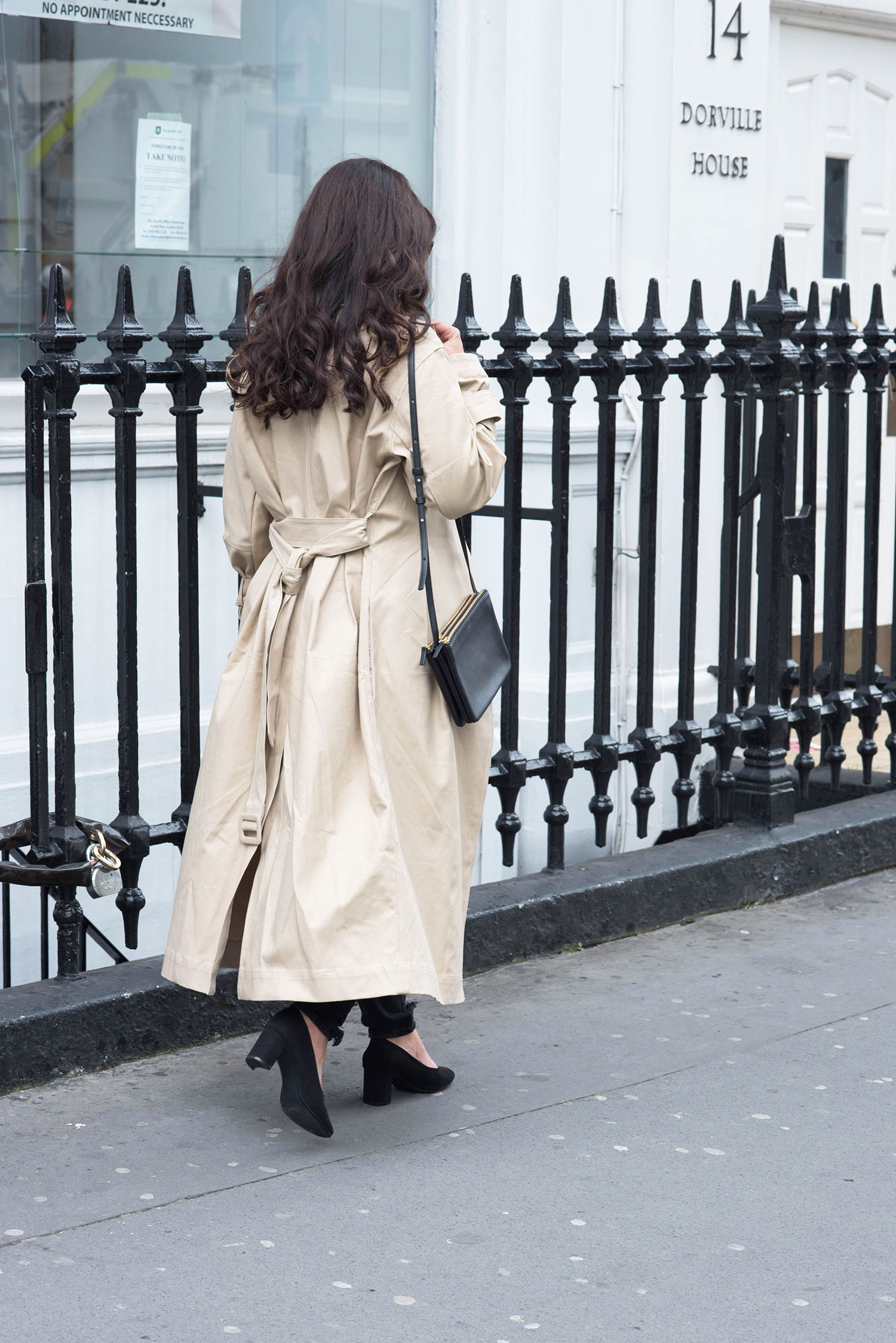 Fashion blogger Cee Fardoe of Coco & Vera walks in London wearing an H&M trench coat and carrying a Celine trio bag