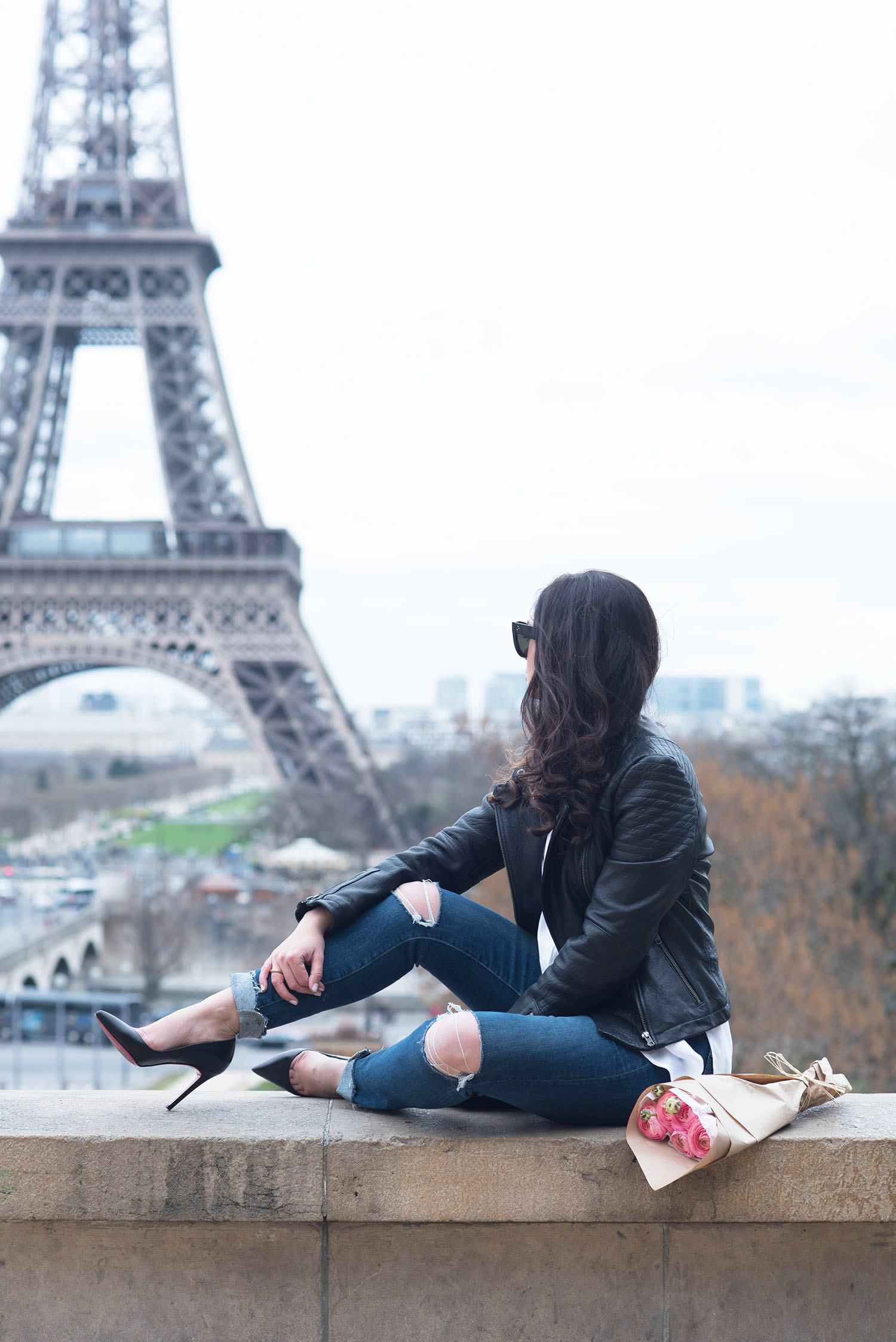 Fashion blogger Cee Fardoe of Coco & Vera sits at Place Trocadero in front of th Eiffel Tower wearing Paige Hoxton jeans and a Cupcakes and Cashmere leather jacket