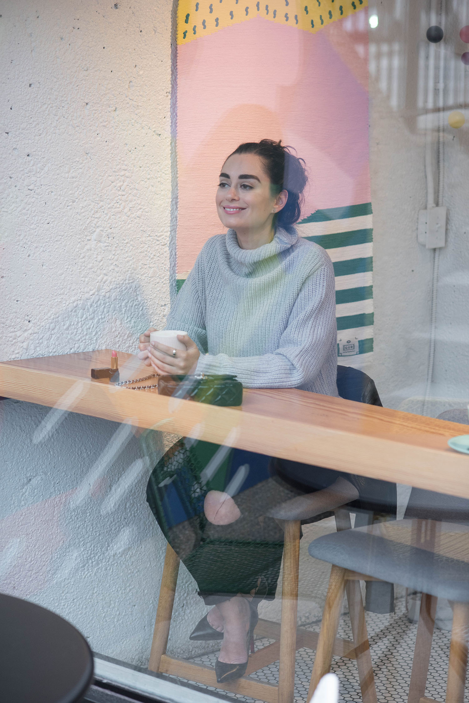 Fashion blogger Cee Fardoe of Coco & Vera sits in the window of Little Sister coffee wearing an grey Aritzia sweater and black paige jeans