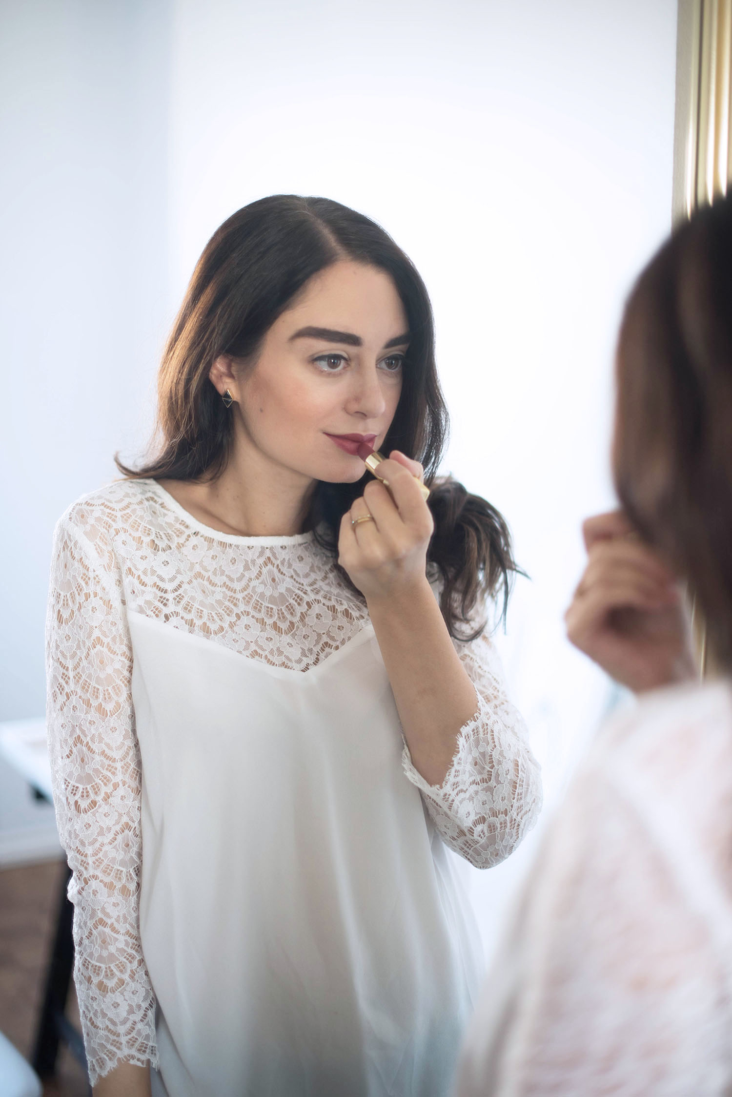 Portrait of brunette fashion blogger Cee Fardoe of Coco & Vera applying Guerlain lipstick while wearing a white Sezane blouse
