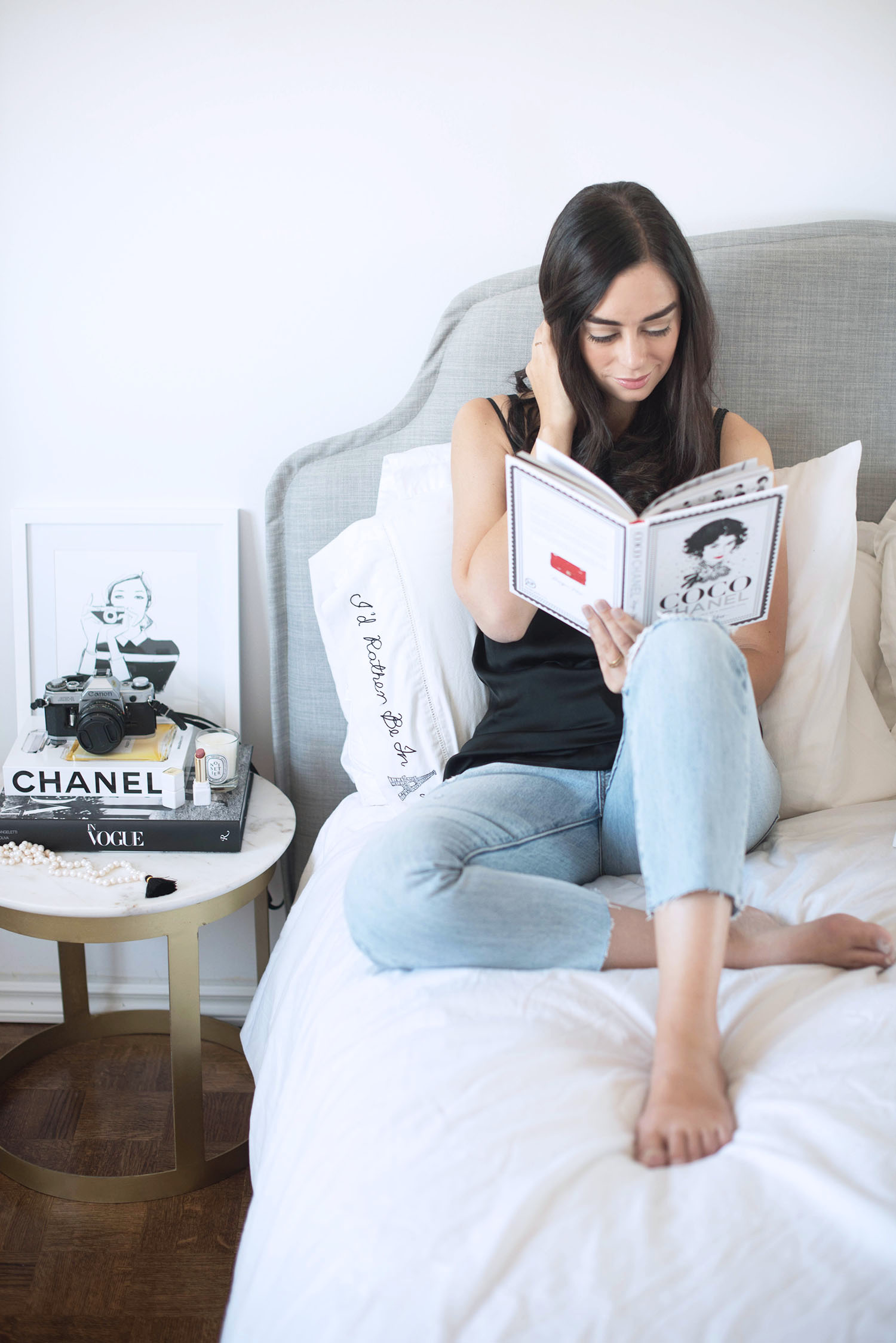 Fashion blogger Cee Fardoe of Coco & Vera sis on her bed reading Coco Chanel by Megan Hess, wearing Levi's jeans and an Aritzia silk tank