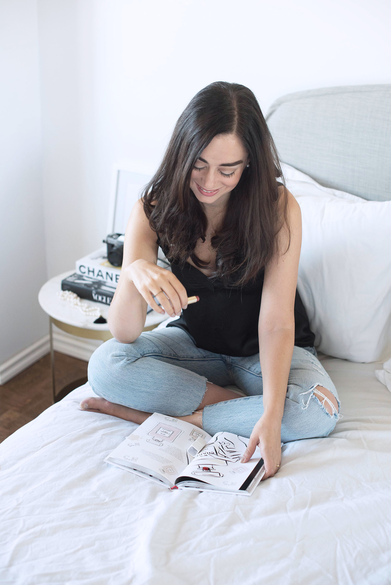 Fashion blogger Cee Fardoe of Coco & Vera sits on her bed wearing Levi's 501 jeans and an Aritzia silk tank, holding a tube of Guerlain lipstick