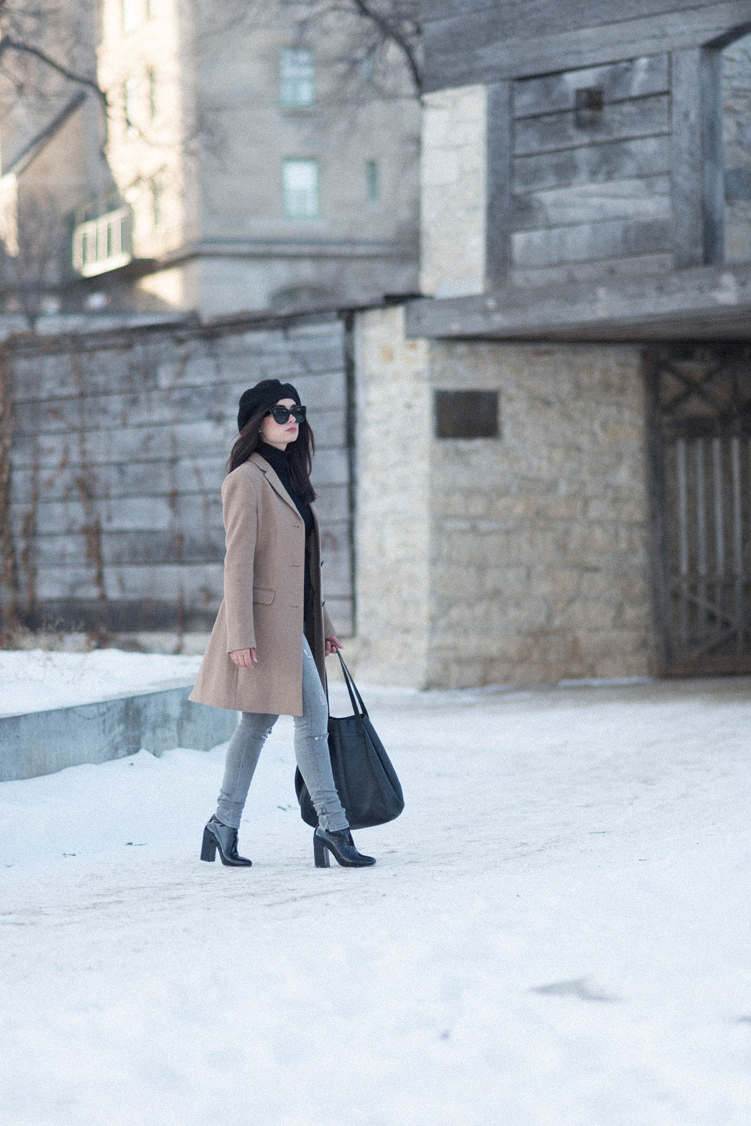 Fashion blogger Cee Fardoe of Coco & Vera walks through the ruins of Fort Garry in Winnipeg wearing a Uniqlo camel coat and Raye patent ankle boots