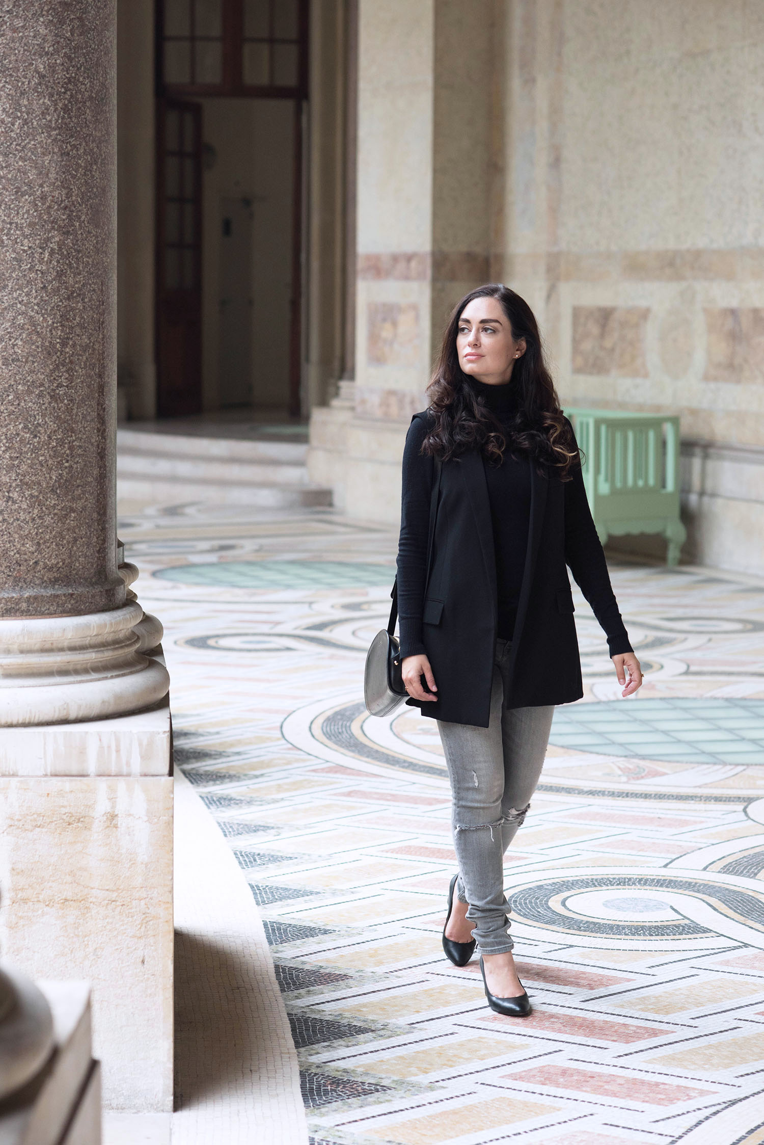 Fashion blogger Cee Fardoe of Coco & Vera walks through the Petit Palais wearing a black Zara waistcoat and grey distressed jeans