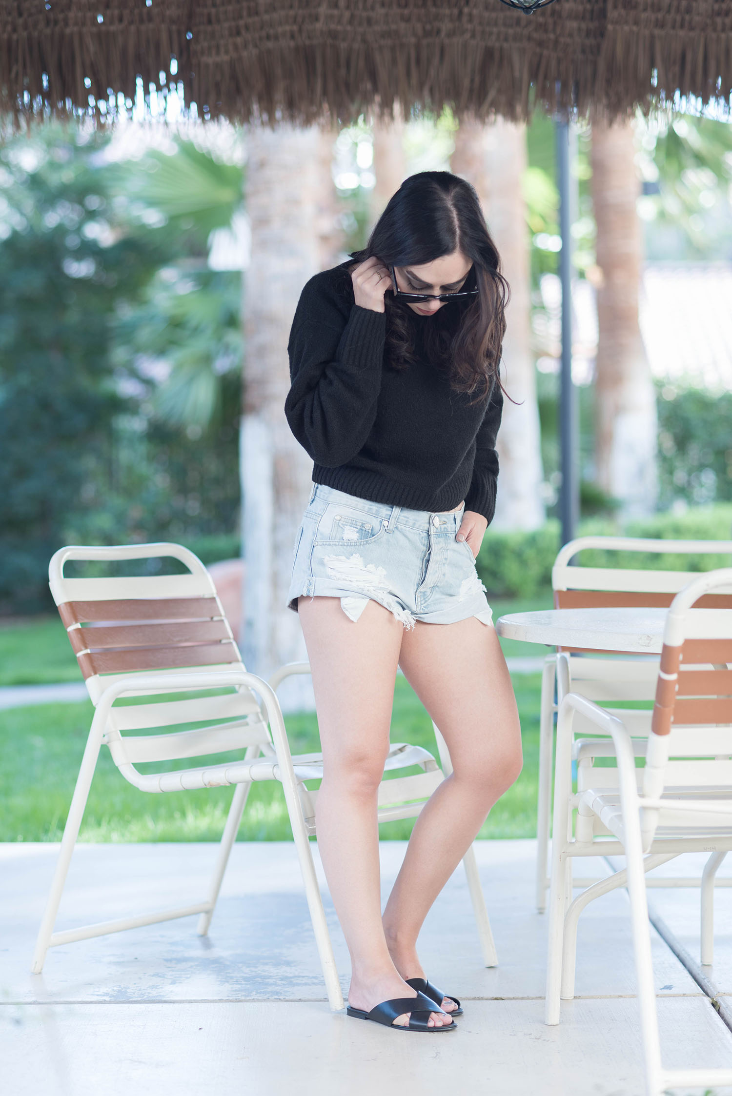 Fashion blogger Cee Fardoe stands inside a cabana in Las Vegas wearing On Teaspoon denim short and an & Other Stories sweater