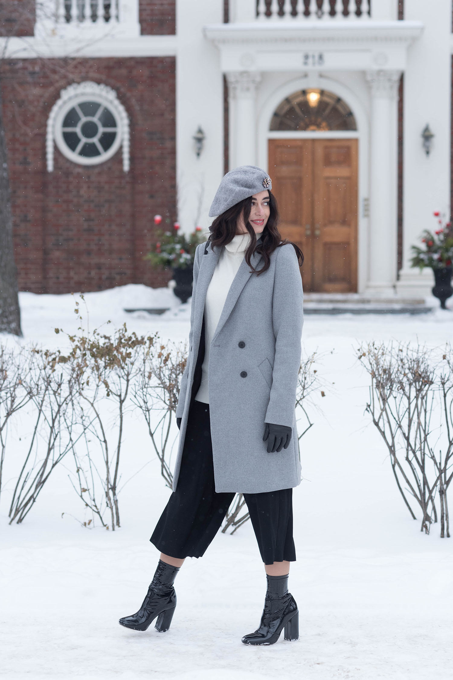 Fashion blogger Cee Fardoe of Coco & Vera walks through the winter snow wearing a Zara coat and Aritzia black culottes