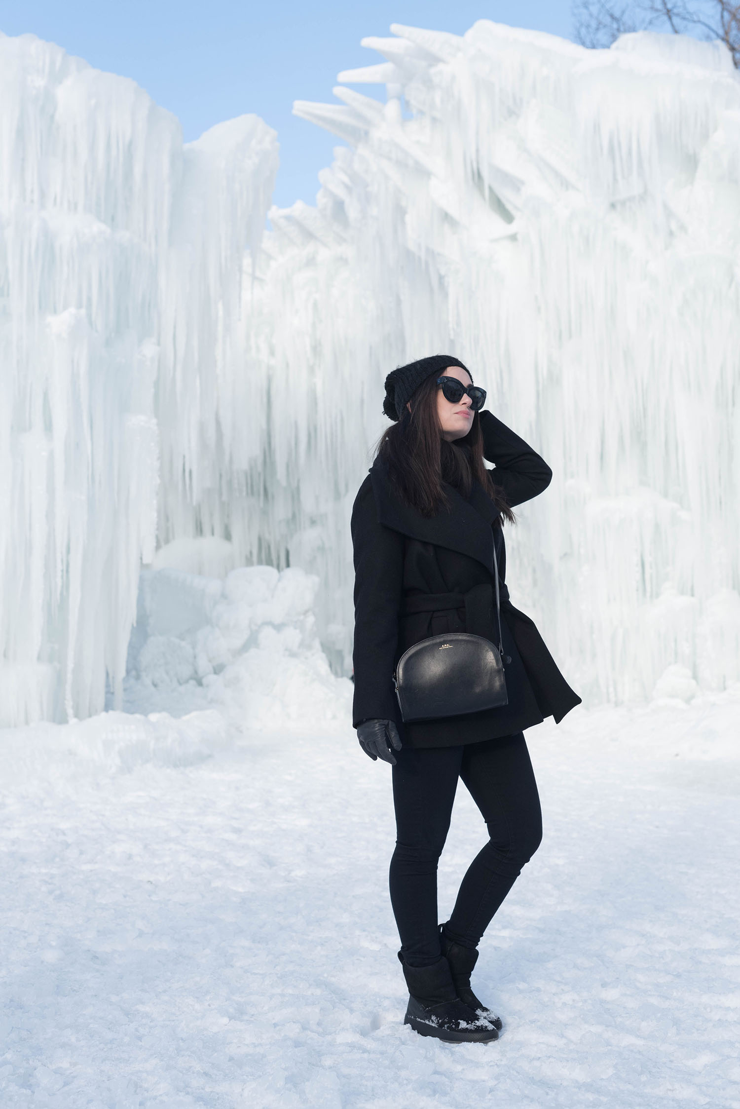 Fashion blogger Cee Fardoe of Coco & Vera stands at Ice Castles at the Forks in Winnipeg wearing a black Mango coat and black Mavi jeans, carrying and APC half moon bag