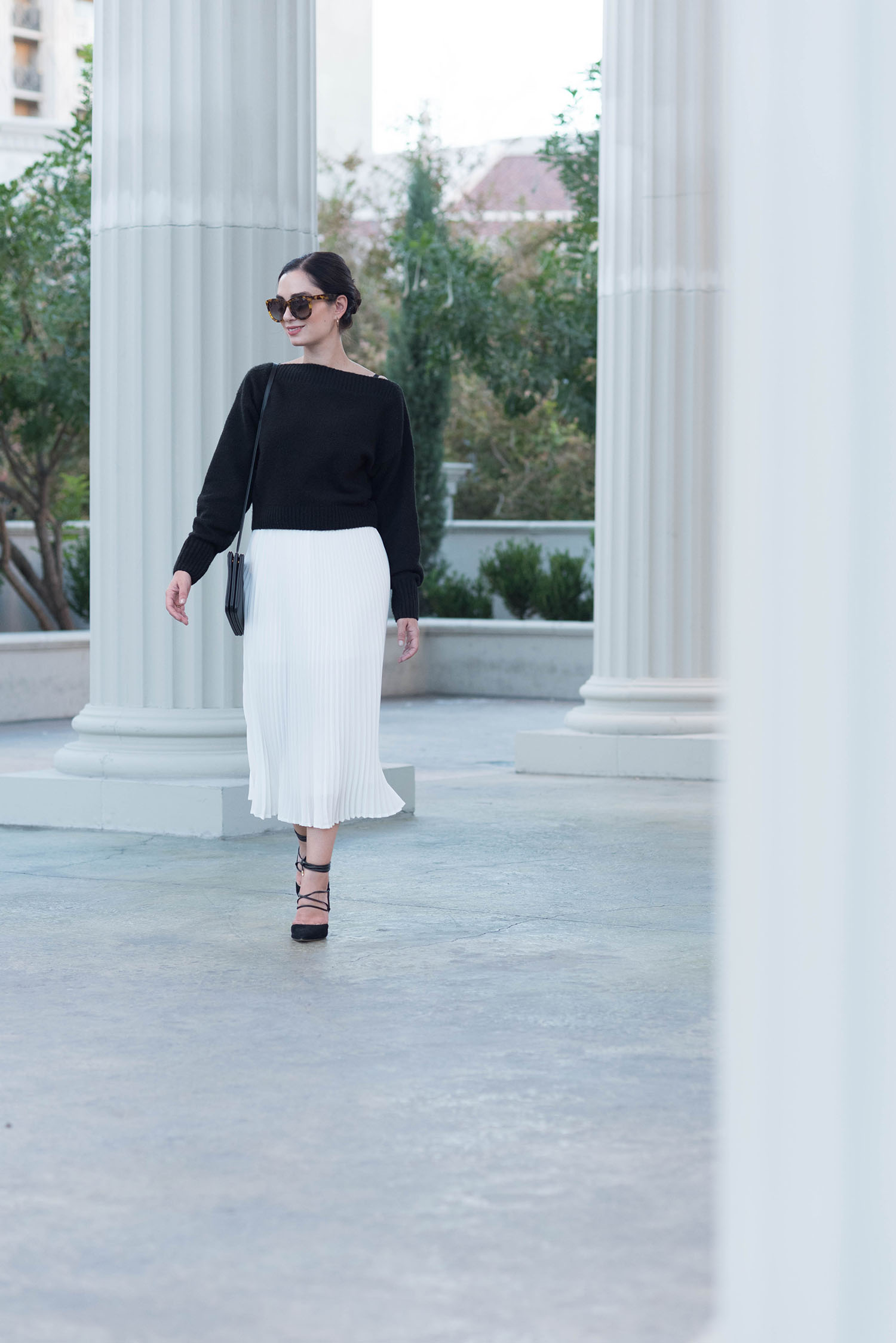 Fashion blogger Cee Fardoe of Coco & Vera walks among the columns at Caesar's Palace in Las Vegas, wearing an & Other Stories sweater and a white pleated skirt