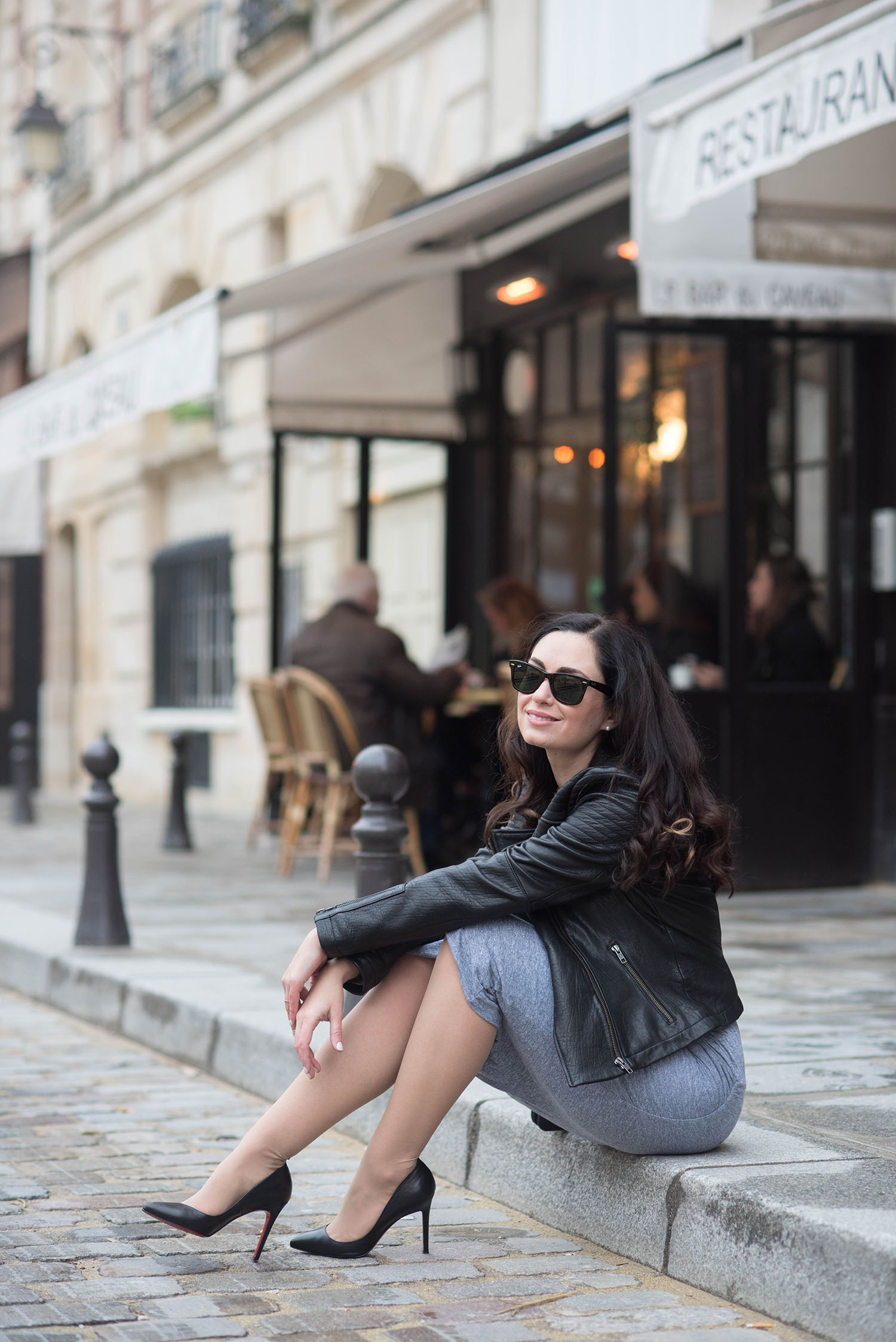 Fashion blogger Cee Fardoe of Coco & Vera sits outside at cafe at Place Dauphine in Paris wearing Christian Louboutin Pigalle pumps and Rayban Wayfarer sunglasses