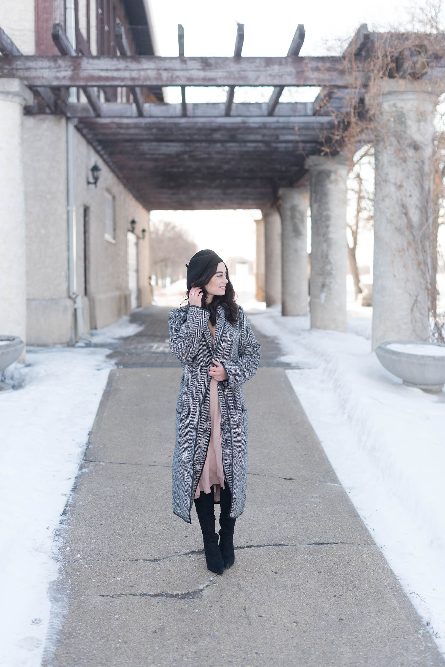 Fashion blogger Cee Fardoe stands outside the Assiniboine Park Pavilion wearing a Lovers + Friends coat and Aldo over the knee boots