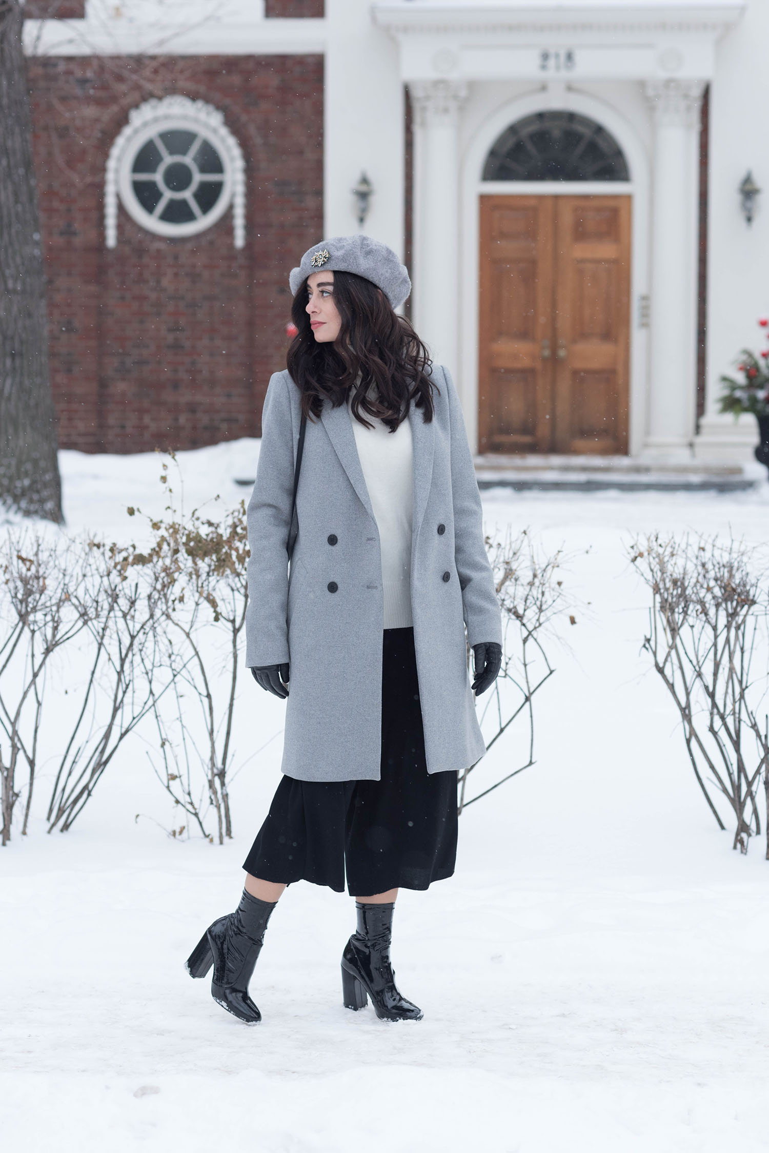 Fashion blogger Cee Fardoe of Coco & Vera walks down Roslyn Road in Winnipeg on a snowy day, wearing a grey Zara coat and Raye patent boots