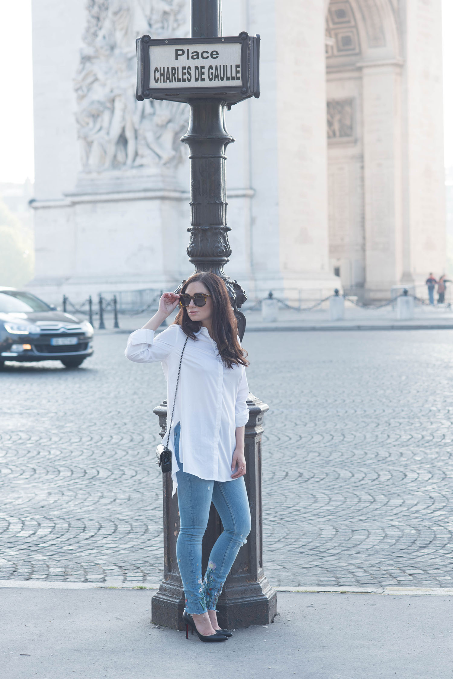 Canadian fashion blogger Cee Fardoe stands near the Arc de Triomphe in Paris wearing Zara embroidered jeans and Christian Louboutin Pigalle pumps