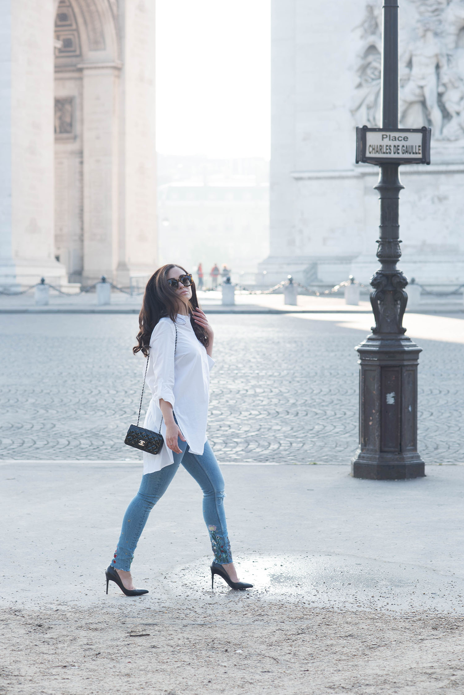 Winnipeg fashion blogger Cee Fardoe of Coco & Vera walks near the Arc de Triomphe in Paris wearing Zara embroidered jeans and carrying a Chanel extra mini handbag