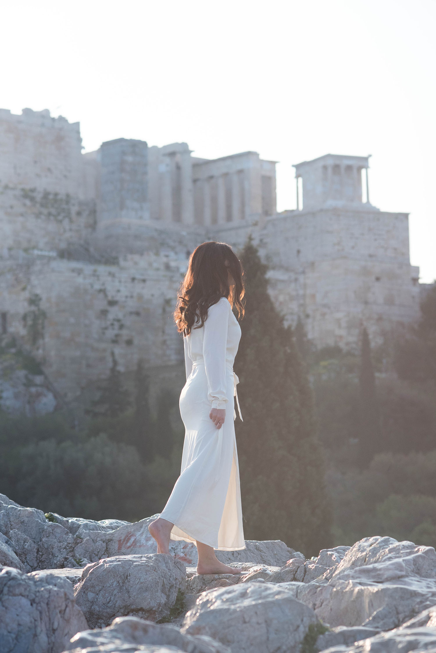 Winnipeg fashion blogger Cee Fardoe of Coco & Vera walks on a rocking outcropping near Acropolis Hill in Greece, wearing a white Lovers + Friends maxi dress