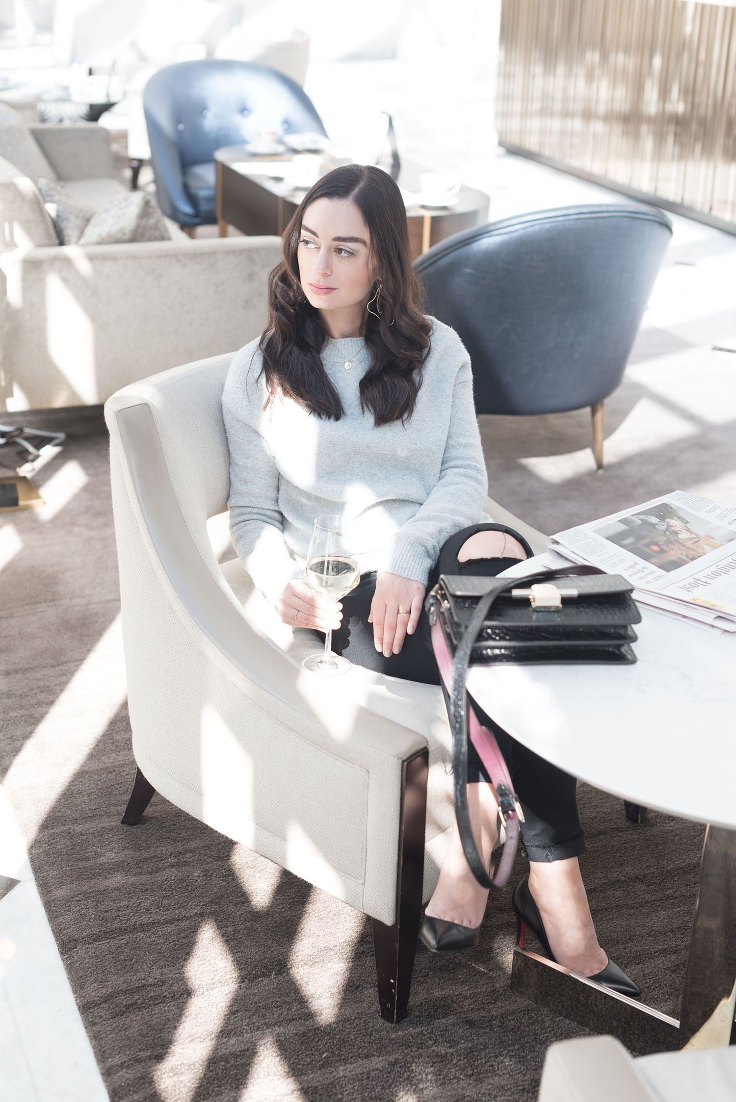 Fashion blogger Cee Fardoe of Coco & Vera sits in the lobby of the Fairmont Washington DC wearing an & Other Stories sweater and Paige black jeans