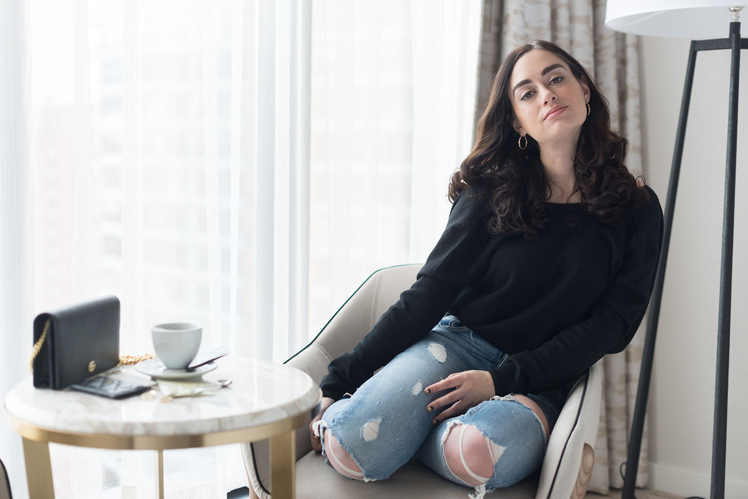 Winnipeg fashion blogger Cee Fardoe sits in a chat at the JW Marriott at Parq Vancouver, wearing Grlfrnd Karolina jeans and Urban Outfitters hoop earrings