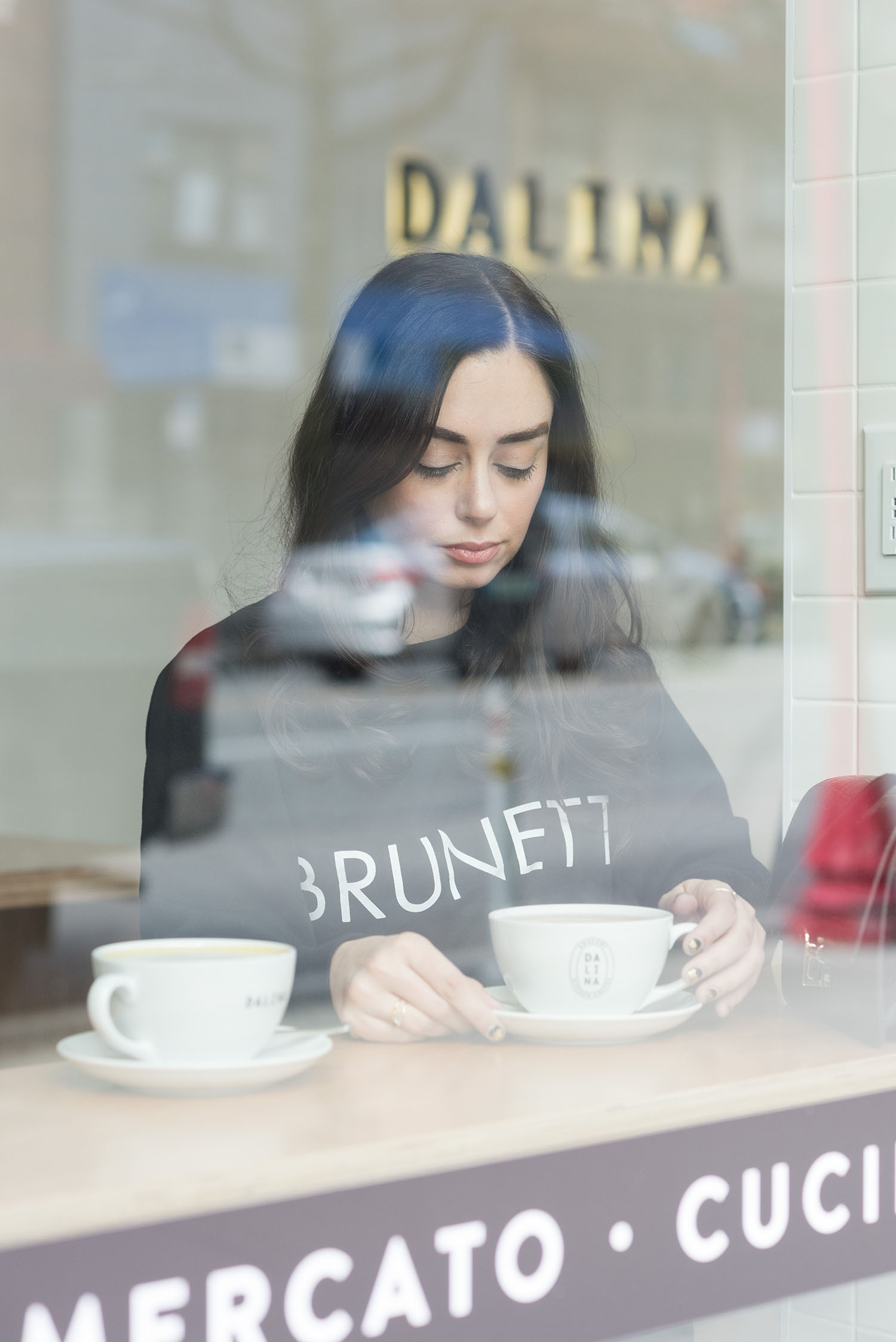 Portrait of fashion blogger Cee Fardoe of Coco & Vera, seen through the front window of Dalina in Vancouver, wearing a Brunette the Label sweatshirt