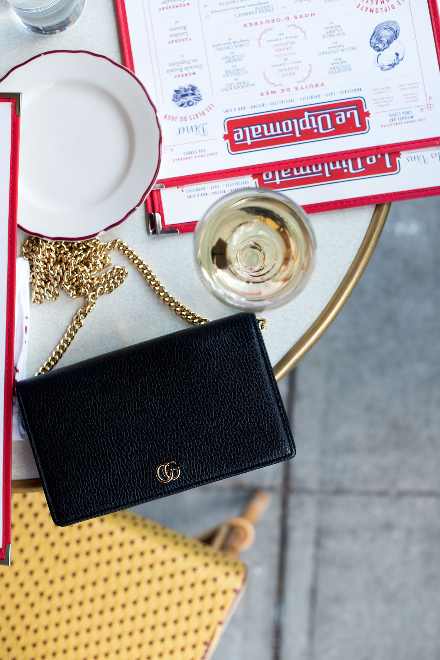 A Gucci marmont black leather bag and a glass of white wine on a table at Le Diplomate in Washington DC, as photographed by Canadian fashion blogger Cee Fardoe of Coco & Vera
