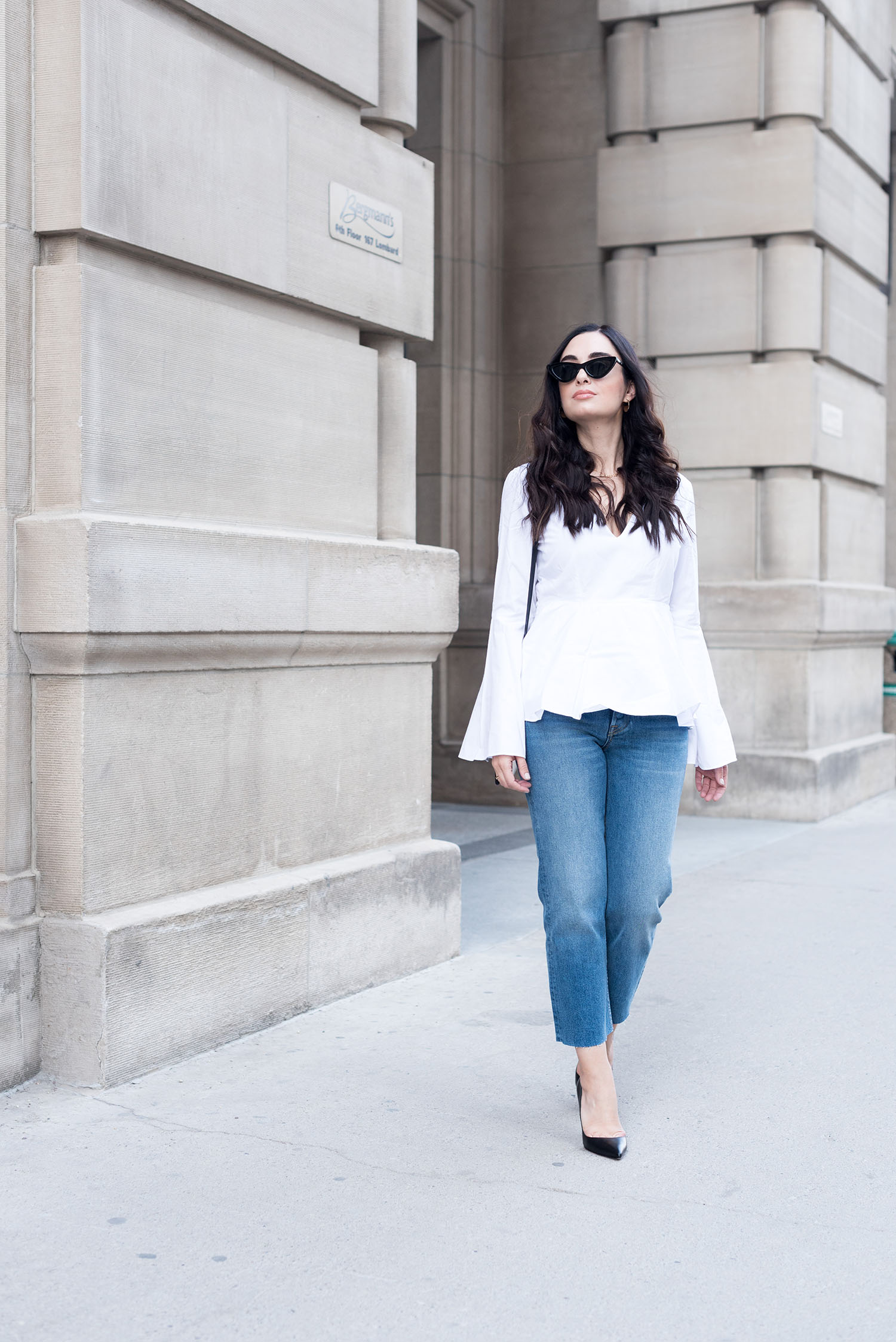Fashion blogger Cee Fardoe of Coco & Vera walks outside the Grain Exchange in Winnipeg wearing a L'Academie blouse and Grlfrnd Helena jeans