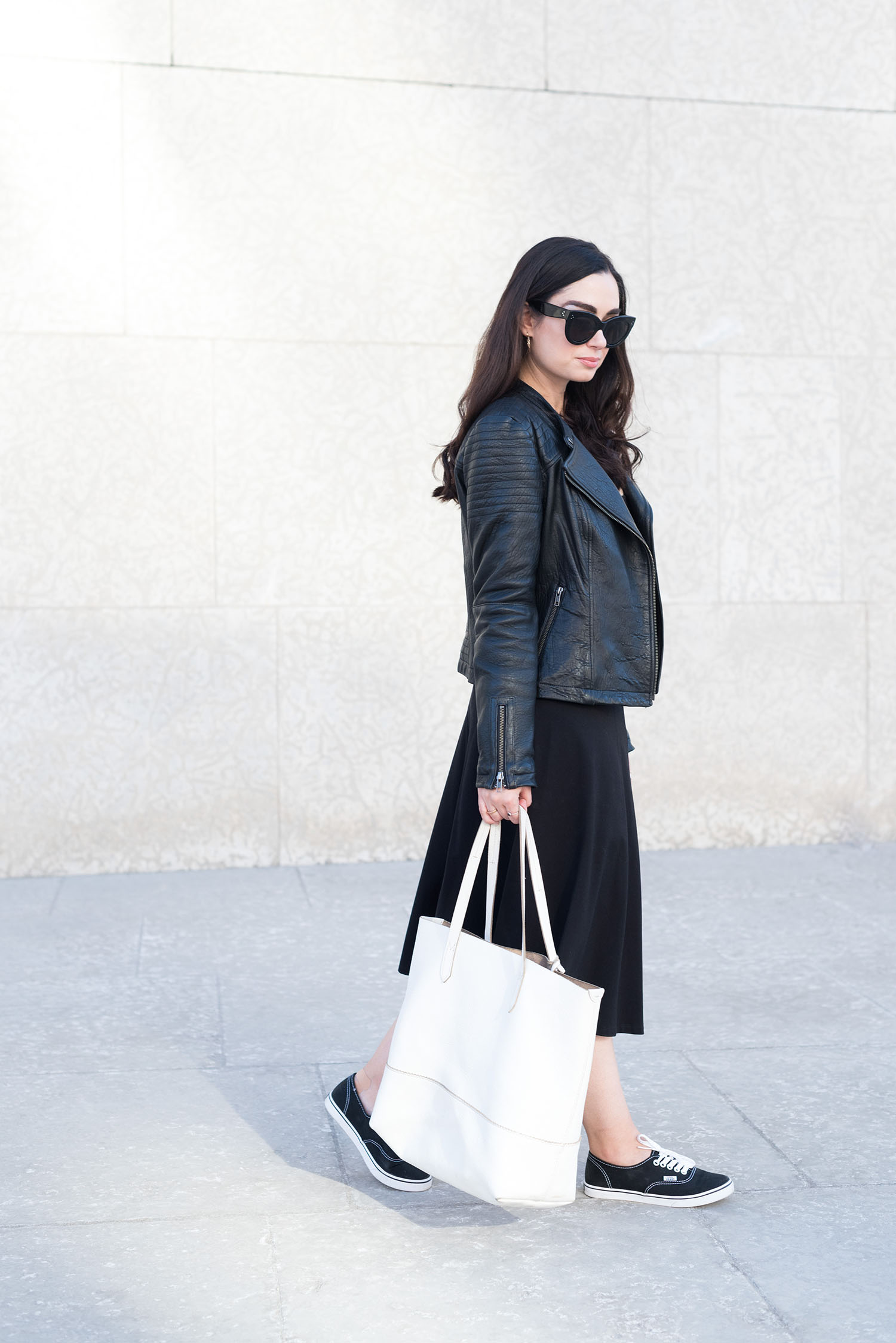 Canadian fashion blogger Cee Fardoe of Coco & Vera walks outside the Winnipeg Art Gallery wearing a black leather jacket and carrying a J. Crew white tote