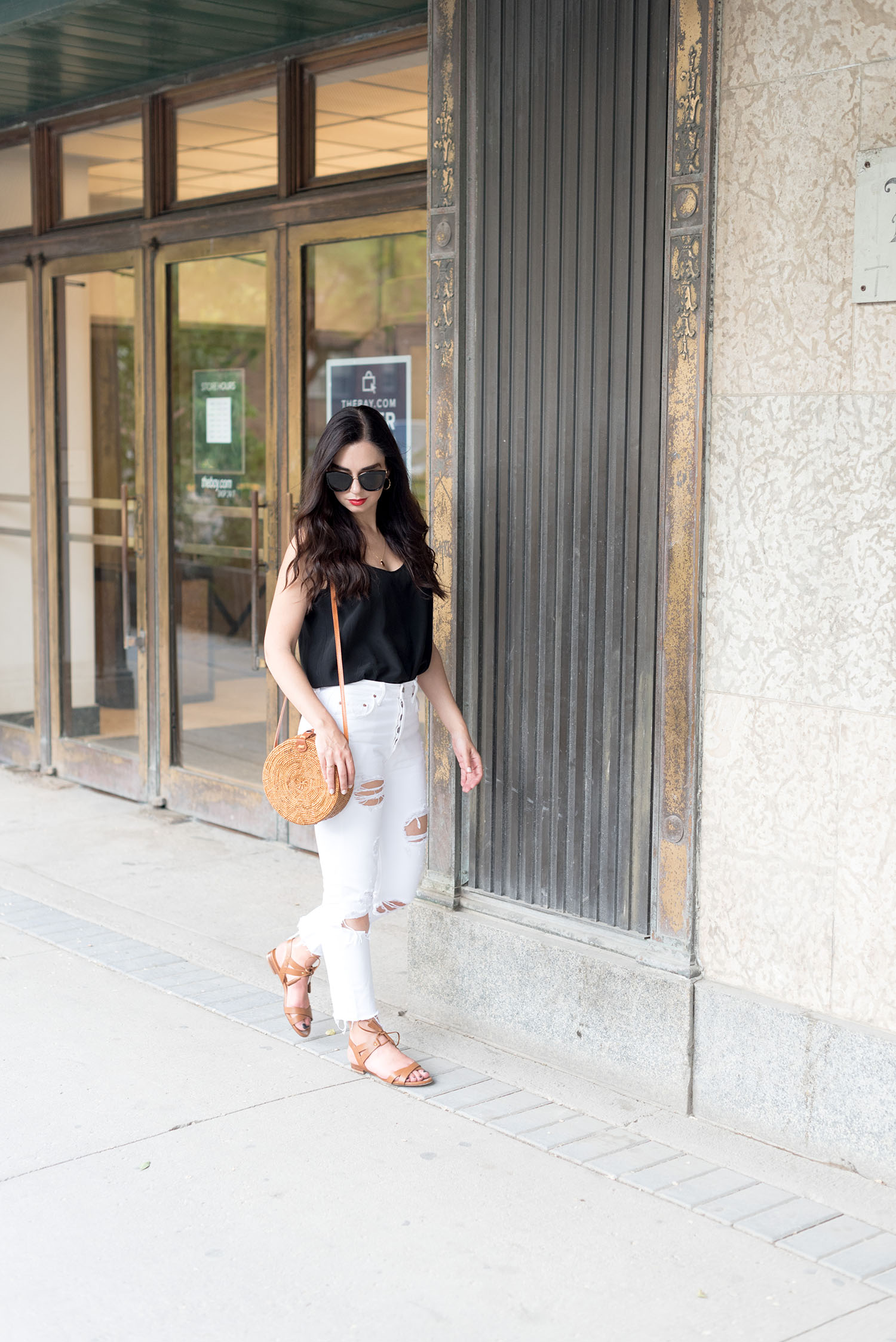 Top Canadian fashion blogger Cee Fardoe of Coco & Vera walks outside The Bay Downtown in Winnipeg, wearing Grlfrnd white jeans and a Sezane silk tank