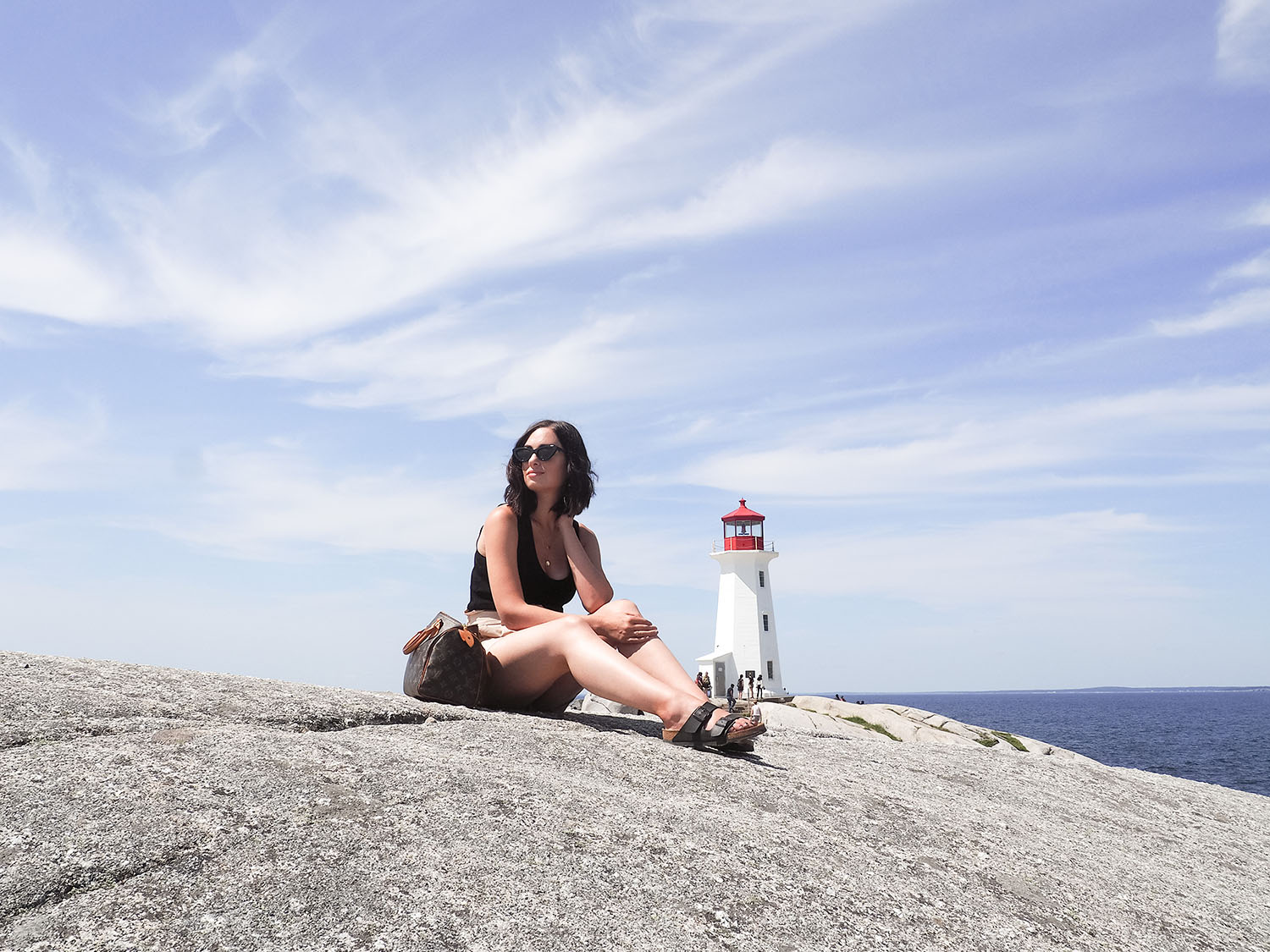 Top Winnipeg travel blogger Cee Fardoe of Coco & Vera sits on the rocks at Peggy's Cove in Nova Scotia