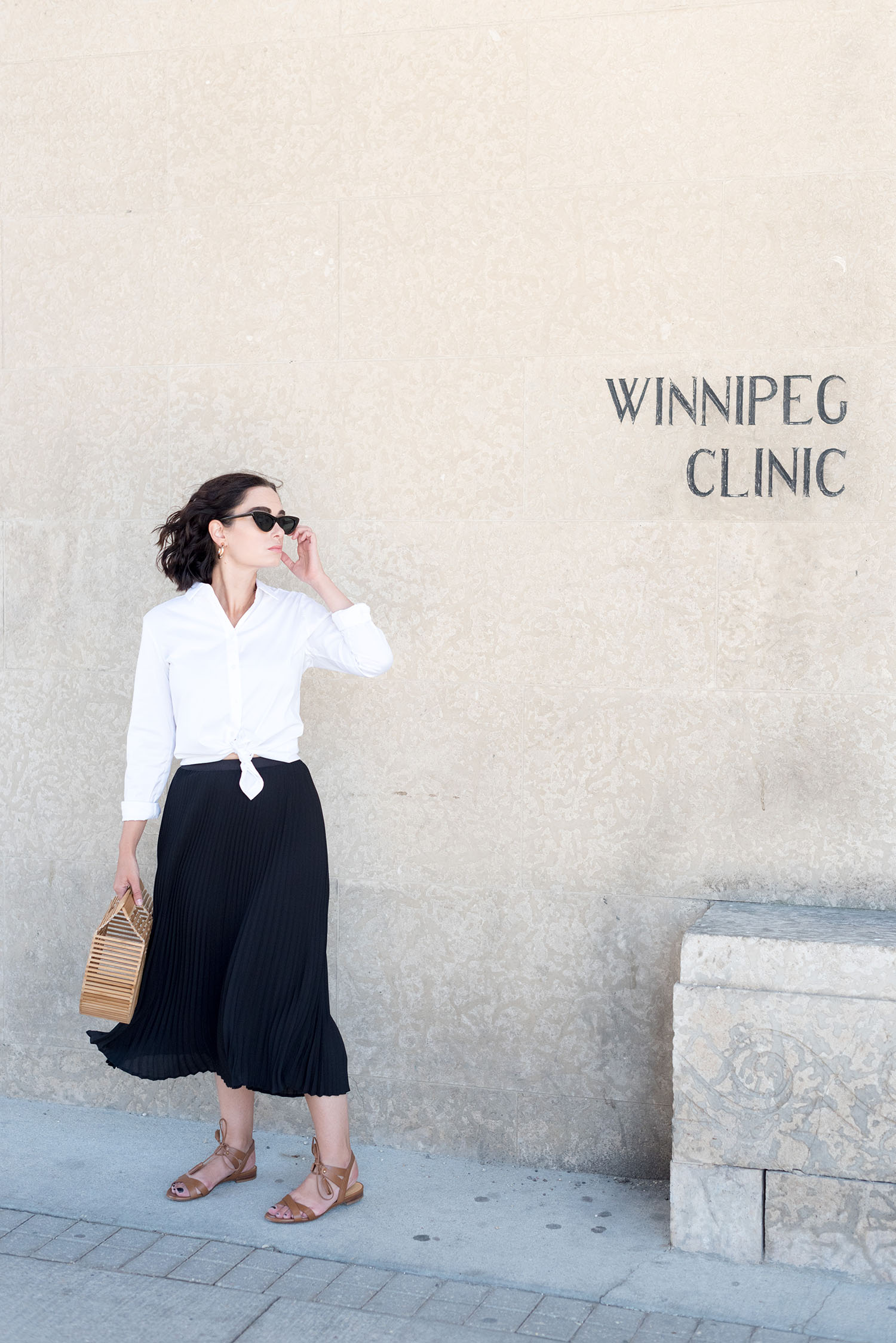 Top Winnipeg fashion blogger Cee Fardoe of Coco & Vera stands outside the Winnipeg Clinic wearing a black pleated skirt from Aritzia and white blouse from Uniqlo