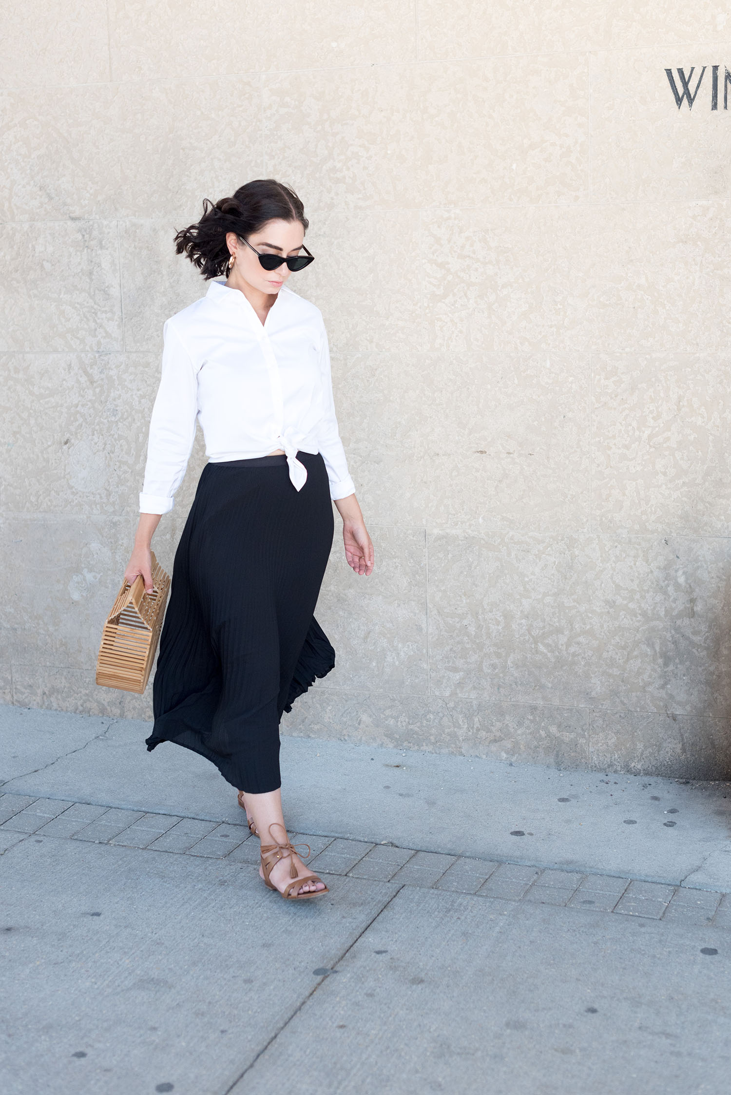 Top Canadian fashion blogger Cee Fardoe of coco & Vera walks outside the Winnipeg Clinic wearing a black pleated skirt from Aritzia and Sezane leather sandals
