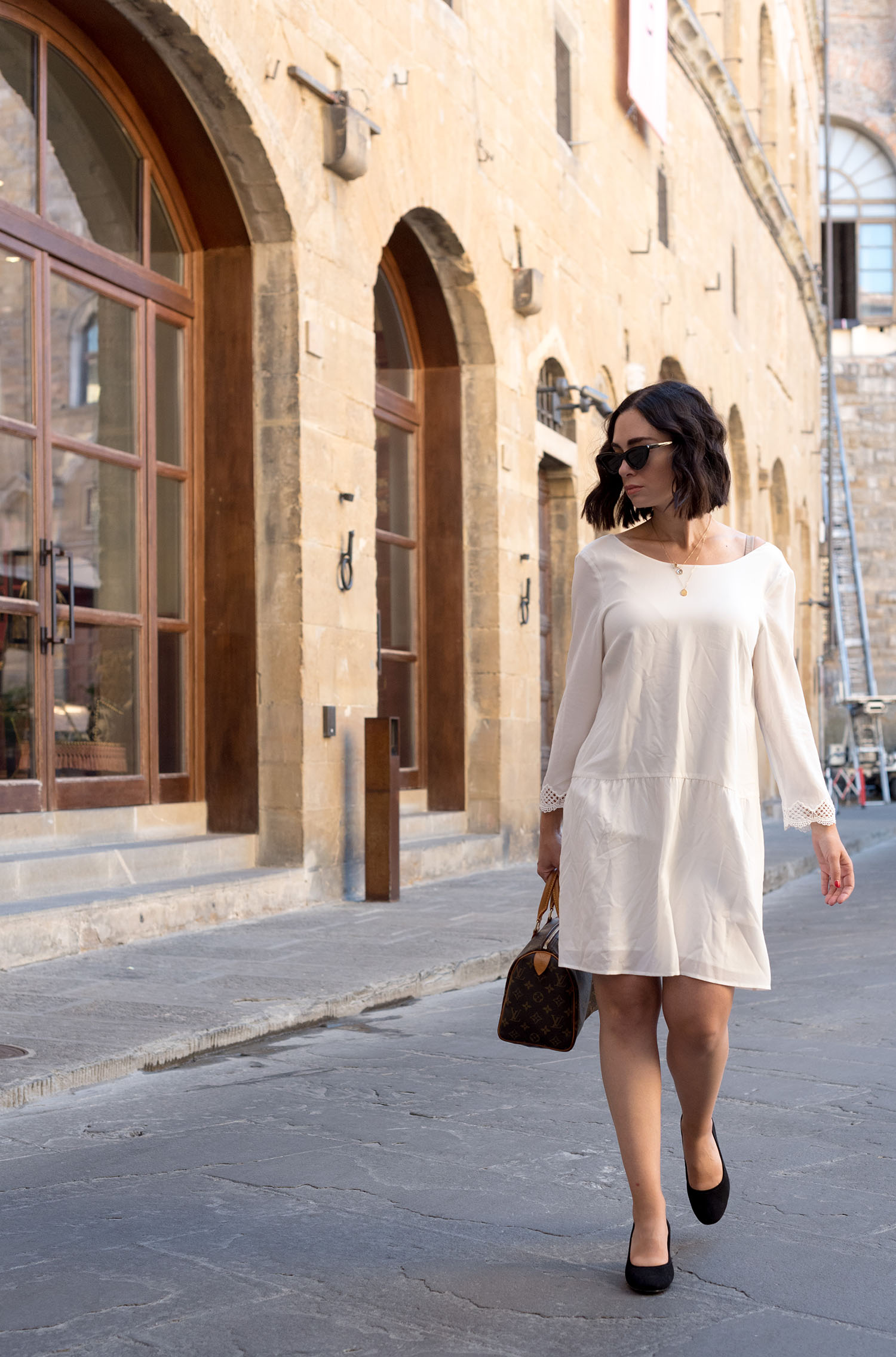 Top Canadian fashion blogger Cee Fardoe of Coco & Vera walks outside Gucci Garden in Florence, Italy, wearing a Sezane white silk dress and H&M block heels