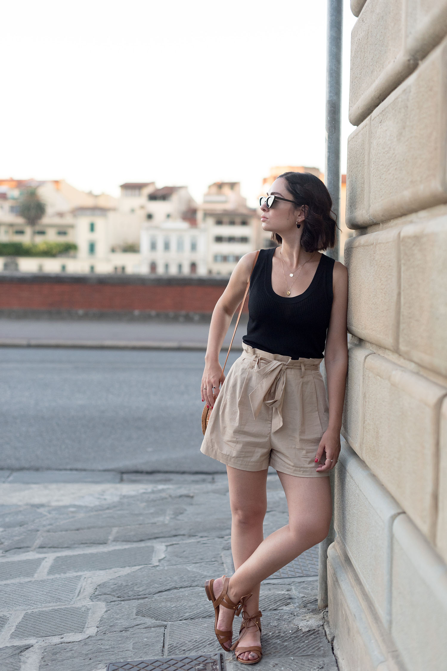 Top Winnipeg travel blogger Cee Fardoe of Coco & Vera stands on the banks of the Arno in Florence, wearing Beige Zara shorts and Sezane sandals