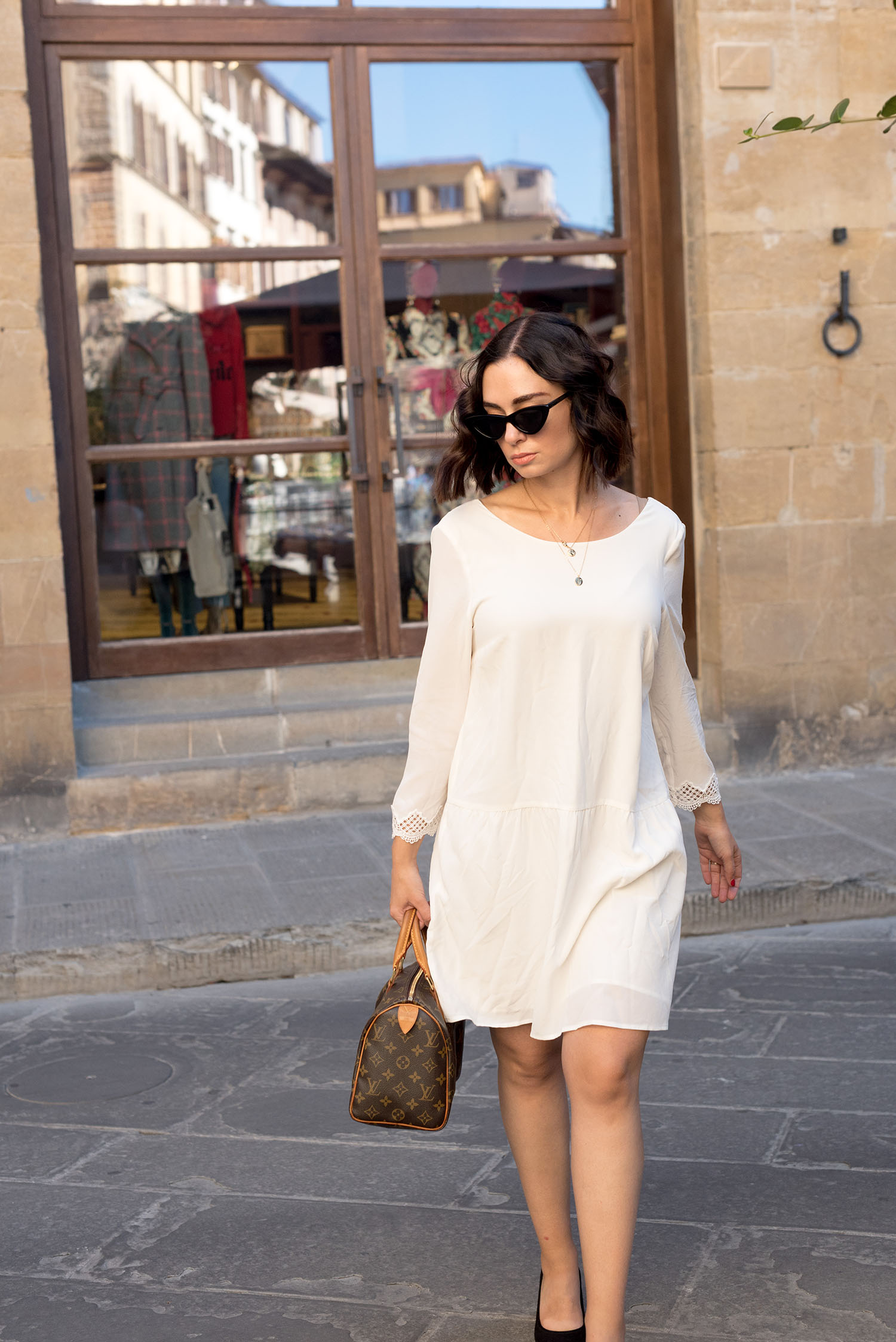Top Canadian fashion blogger Cee Fardoe of Coco & Vera walks outside Gucci Garden in Florence, Italy, wearing a Sezane white silk dress and carrying a Louis Vuitton handbag