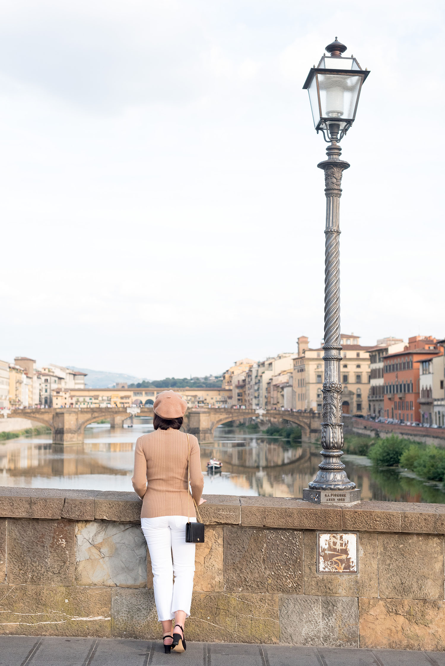 Top Winnipeg fashion blogger Cee Fardoe of Coco & Vera looks out over the Arno River in Florence, Italy, wearing white Mavi jeans and carrying a Gucci Marmont handbag